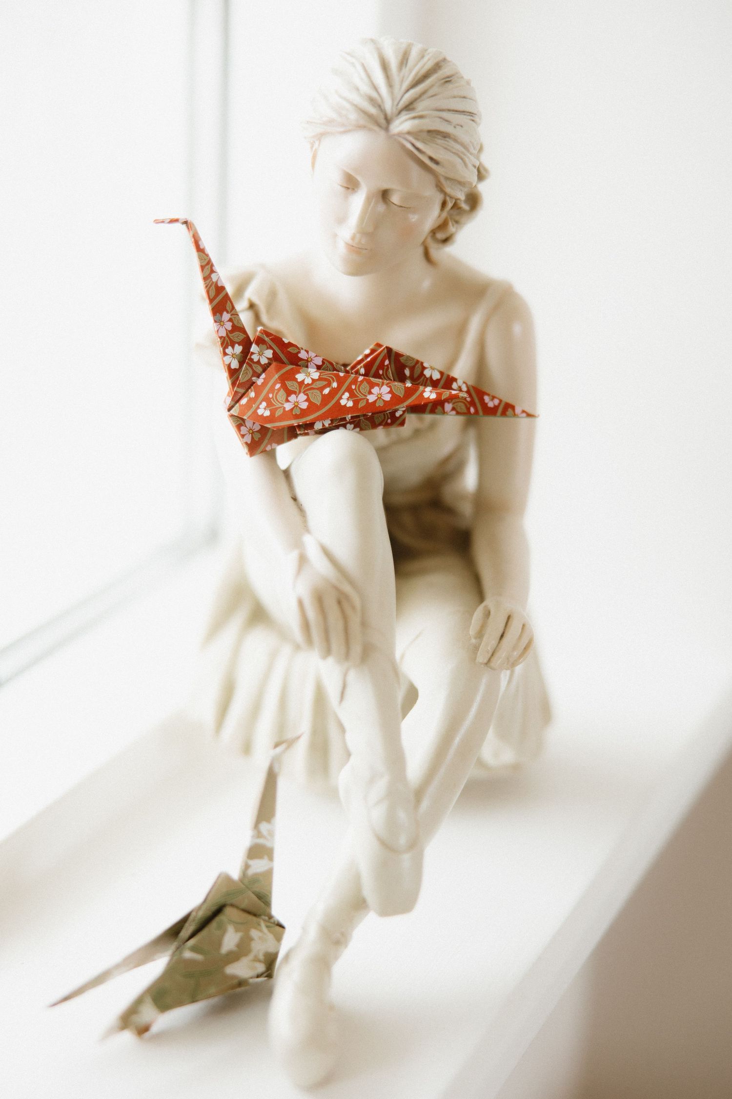 White marble sculpture with red origami accent in dramatic lighting by window.