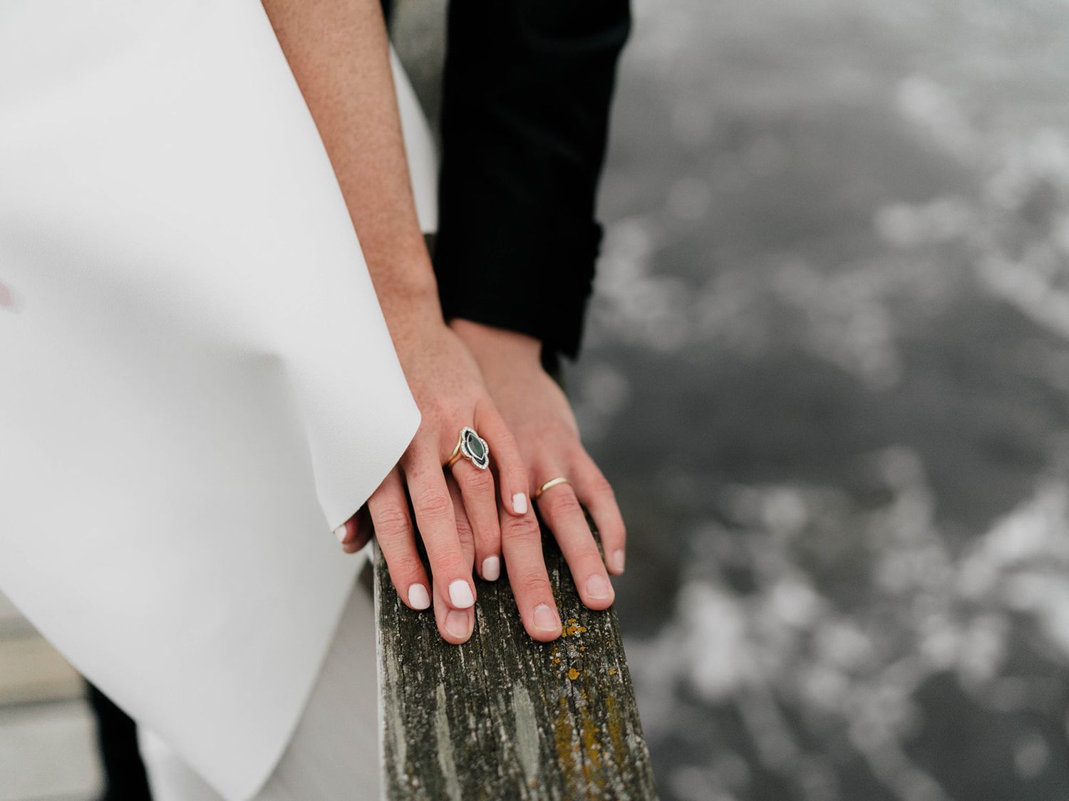 Close-up of hands with wedding rings resting on weathered wood.