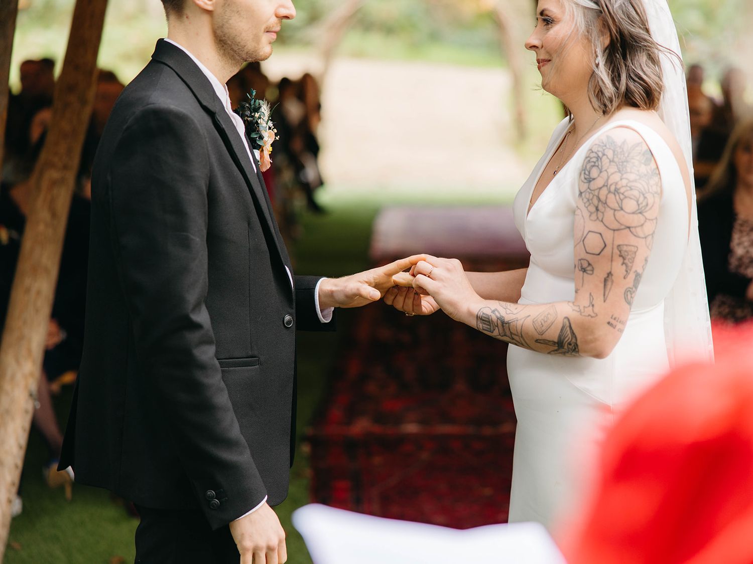 A couple exchanges rings during an intimate outdoor wedding ceremony with the bride wearing a long-sleeved lace gown.