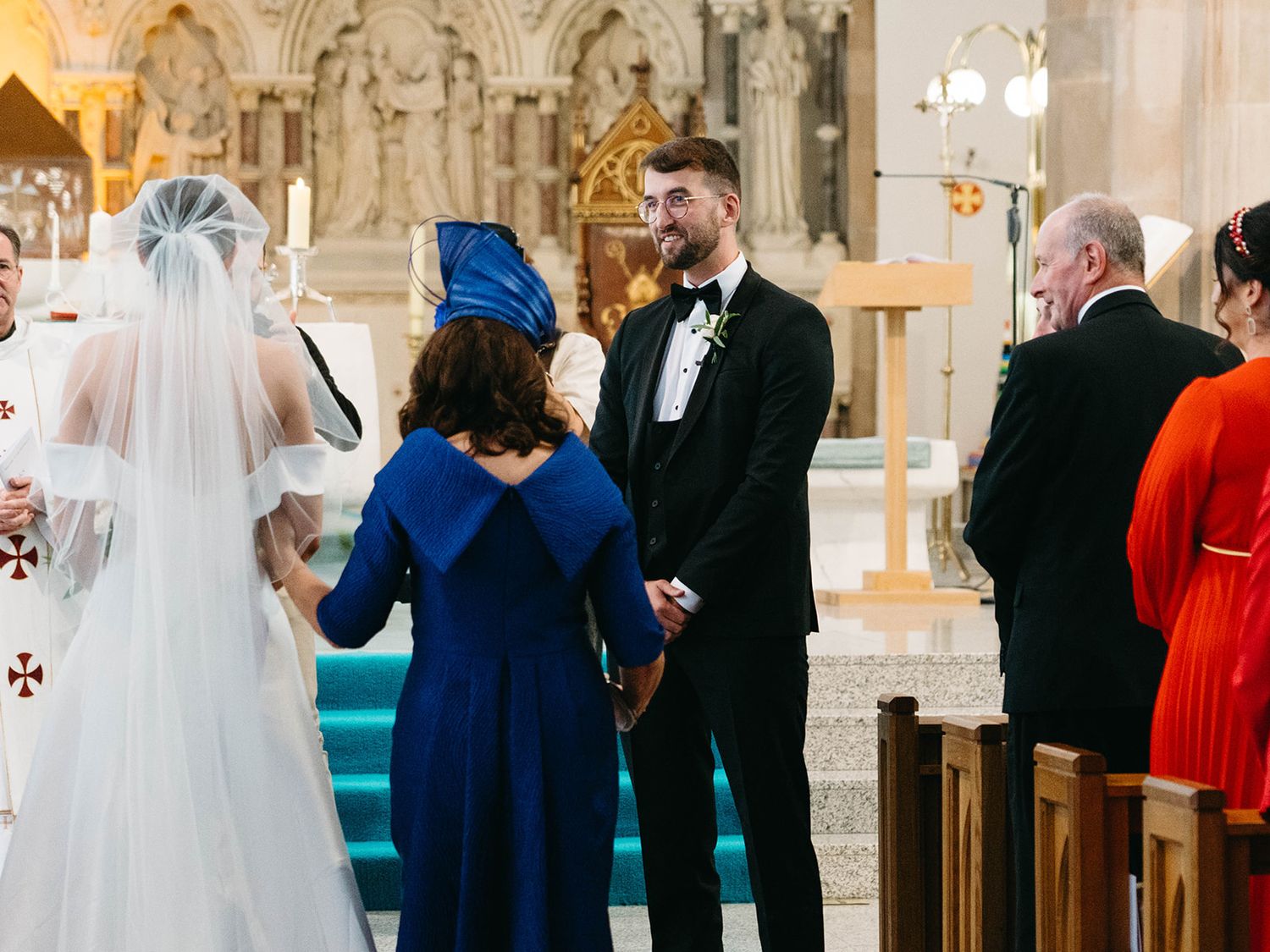 A traditional wedding ceremony takes place inside an ornate church with stone archways and glowing chandeliers.