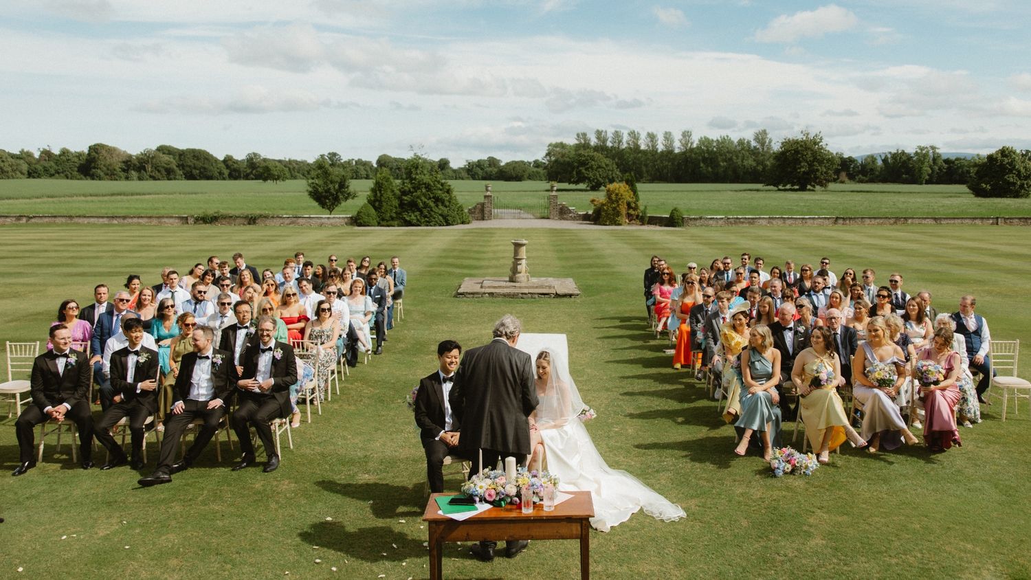 Outdoor wedding ceremony on a lush green golf course with guests seated on white chairs facing the altar area.