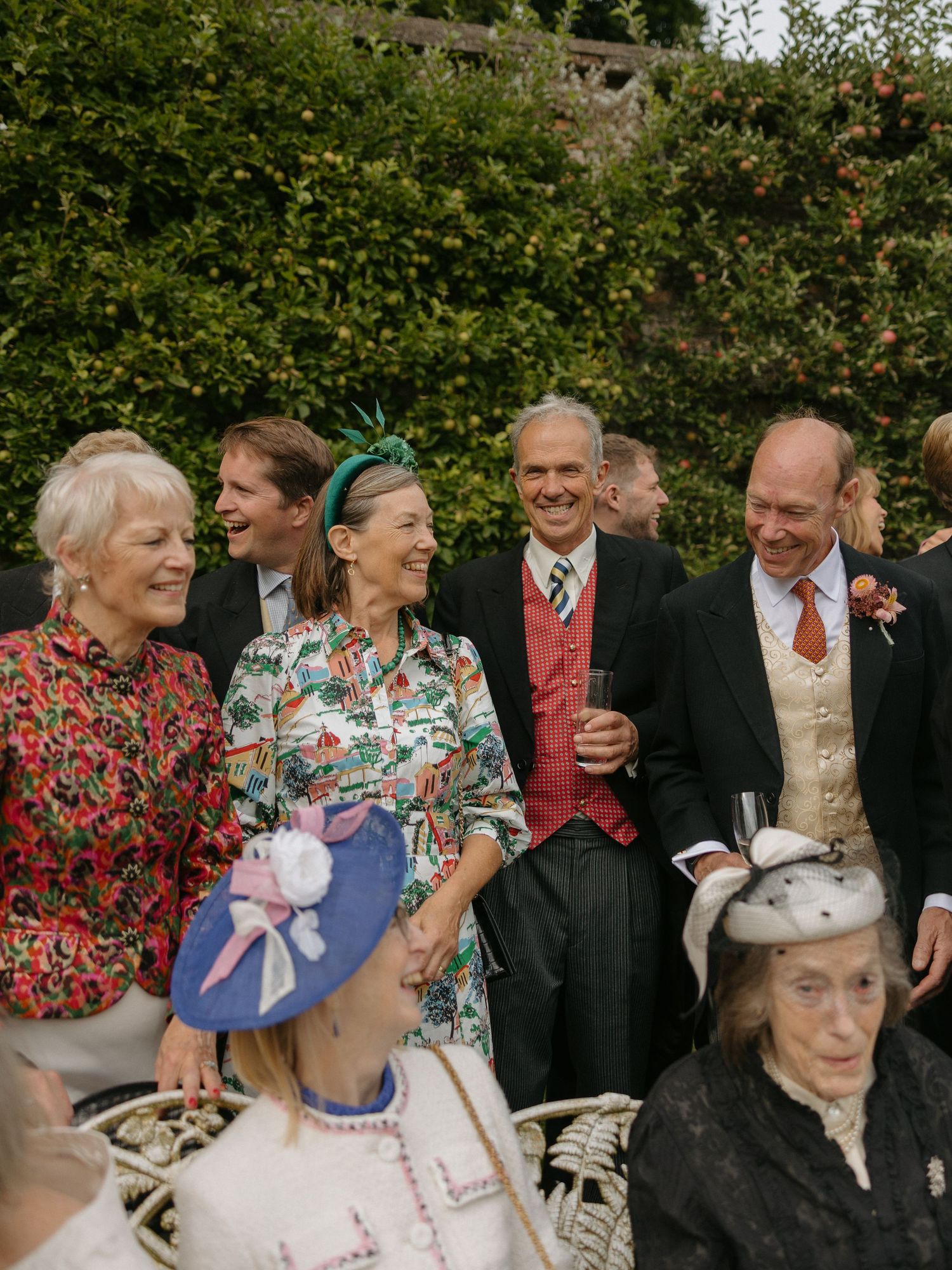 A group of wedding guests enjoying a joyful moment together in a garden setting with lush greenery in the background.