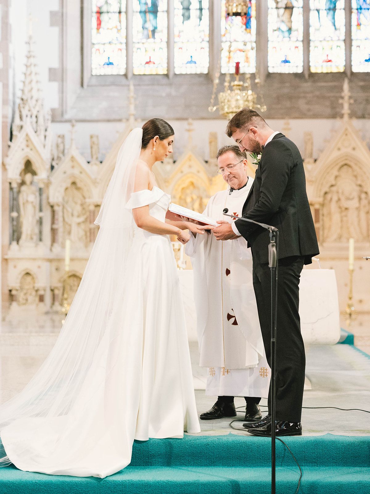 A traditional church wedding ceremony taking place at an ornate altar with stained glass windows in the background.