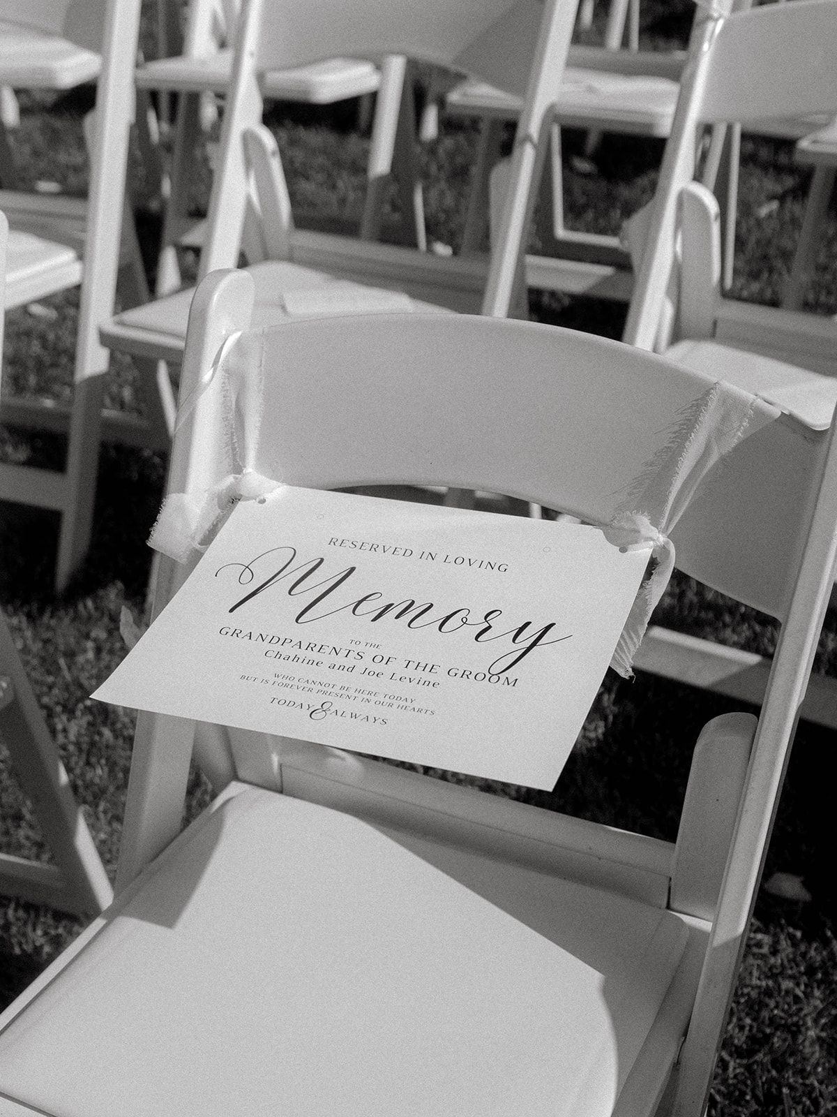 A black and white photo of a reserved memory sign on a white folding chair at a ceremony.
