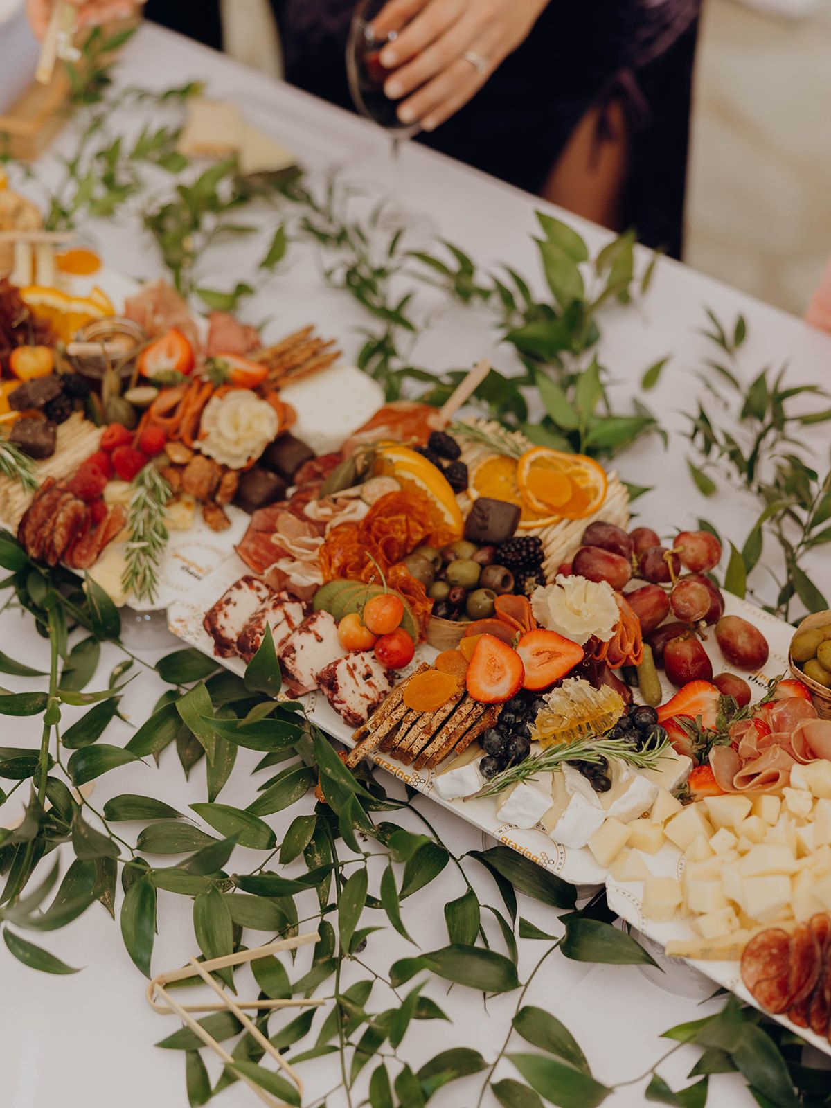 An elegant charcuterie board with meats, cheeses, fruits and nuts decorated with green olive branches on a white platter.