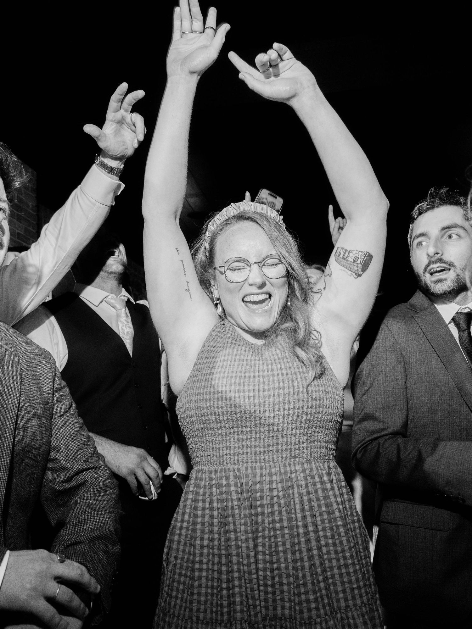 Black and white photo of joyful celebration with dancing and raised arms at a party.