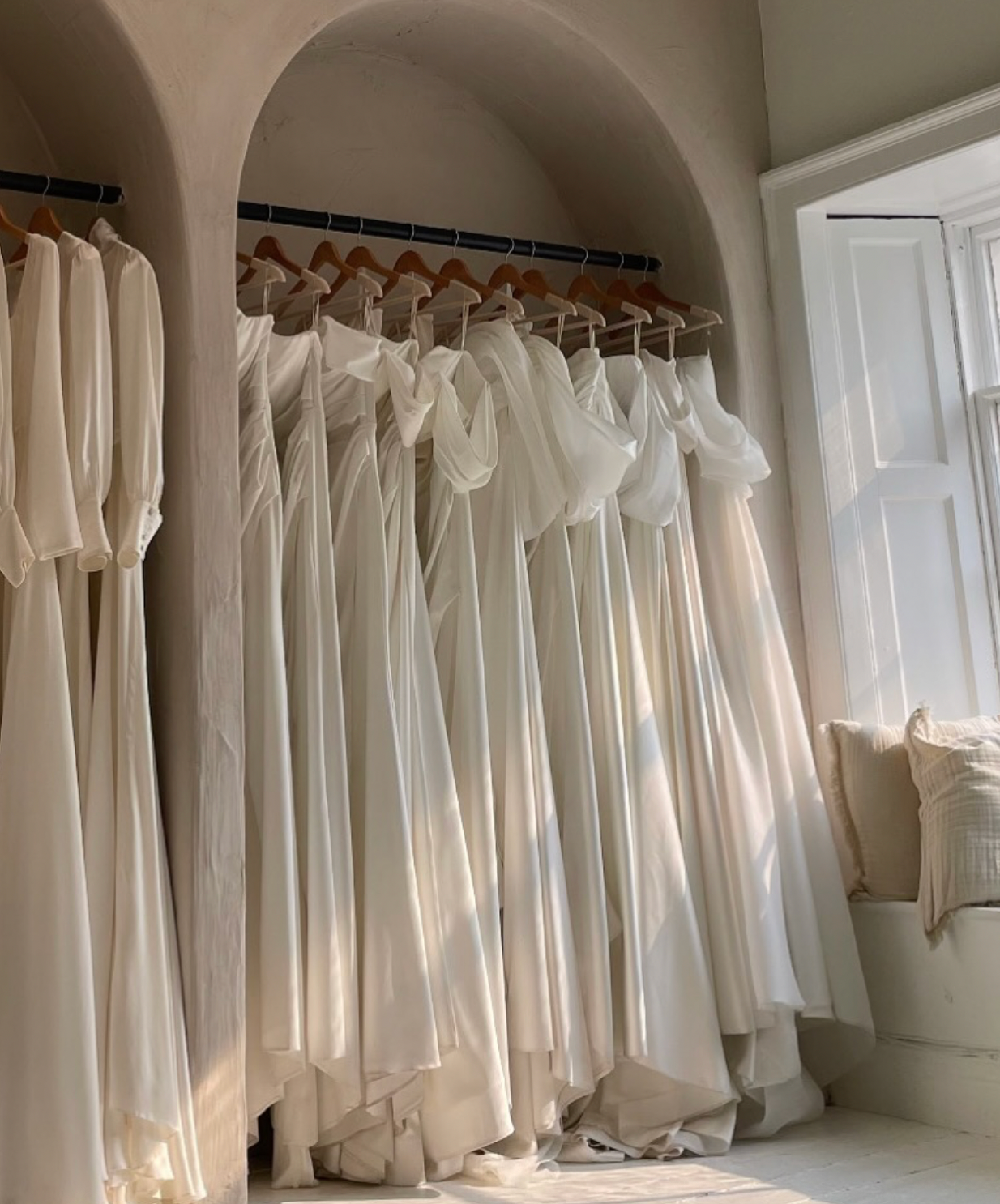 White linen dresses and garments hanging neatly on wooden hangers in a bright, minimalist closet space.