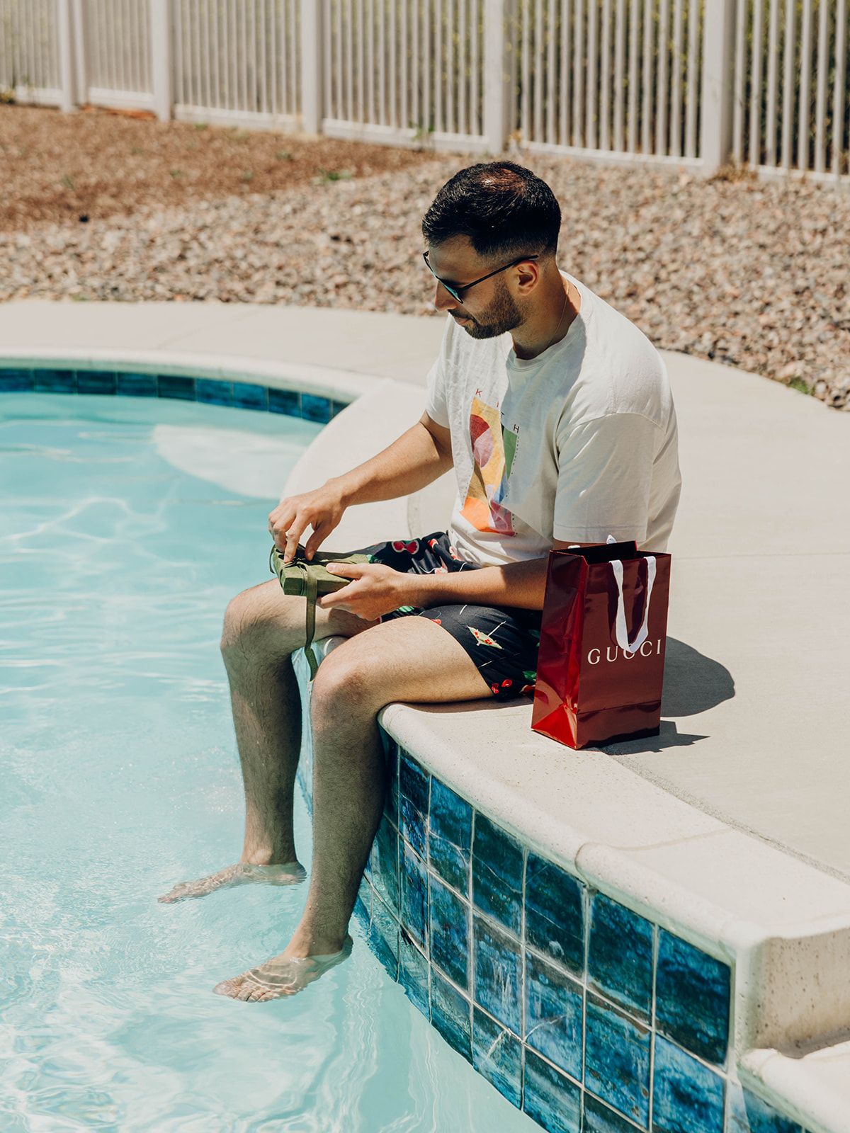 Person relaxing by the pool during summer while sitting on edge with shopping bag and dipping feet in water.