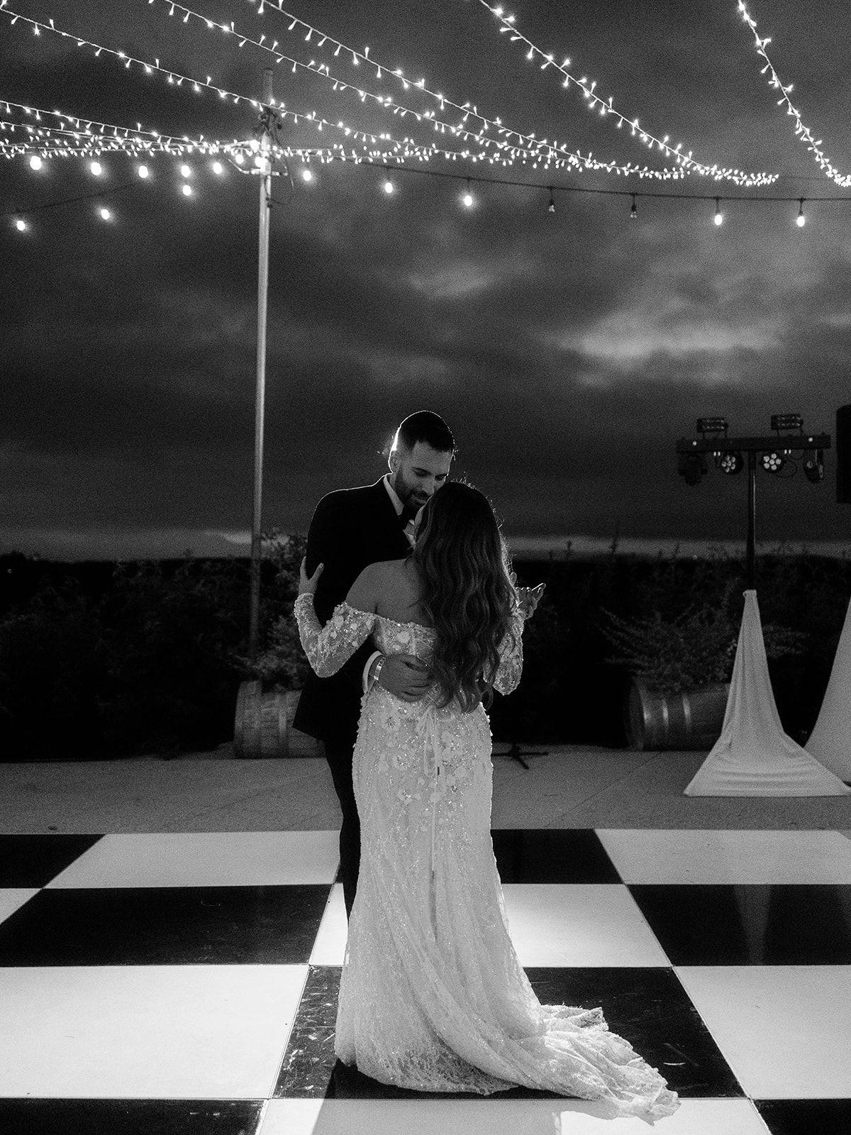 Couple dancing under string lights on a black and white checkered dance floor at night.