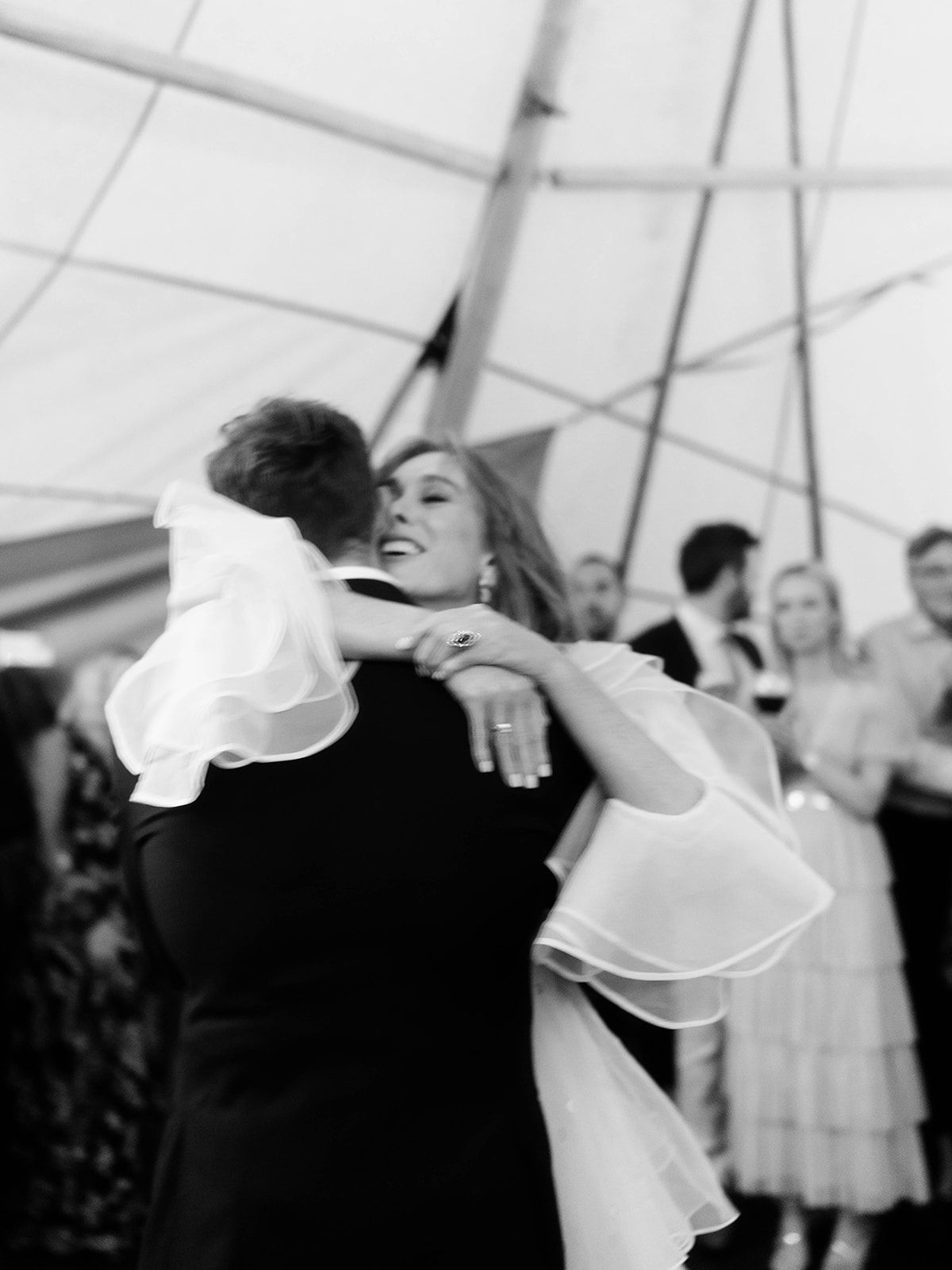 A couple dances together under a white tent at an elegant wedding celebration.