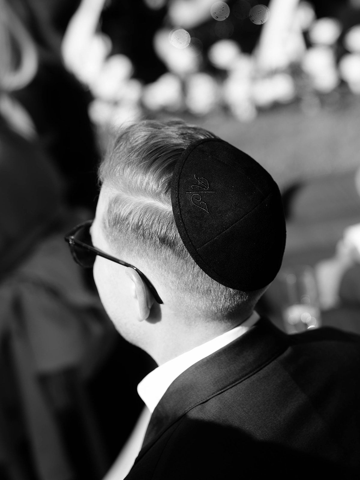 Black and white view of someone wearing a yarmulke and suit, showing the back of their head at what appears to be a formal event.