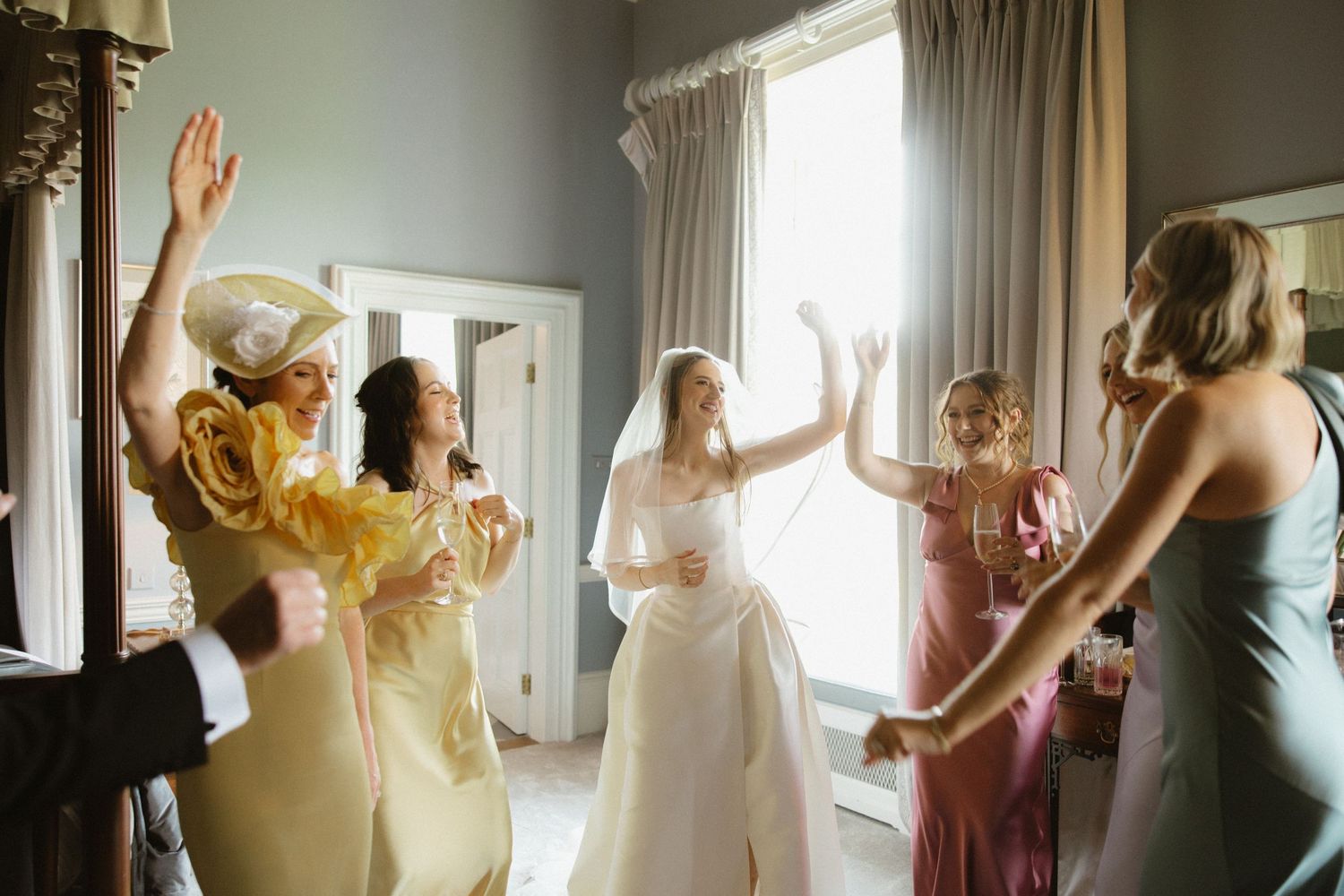 A celebratory moment with a group dancing in formal attire by a sunlit window.