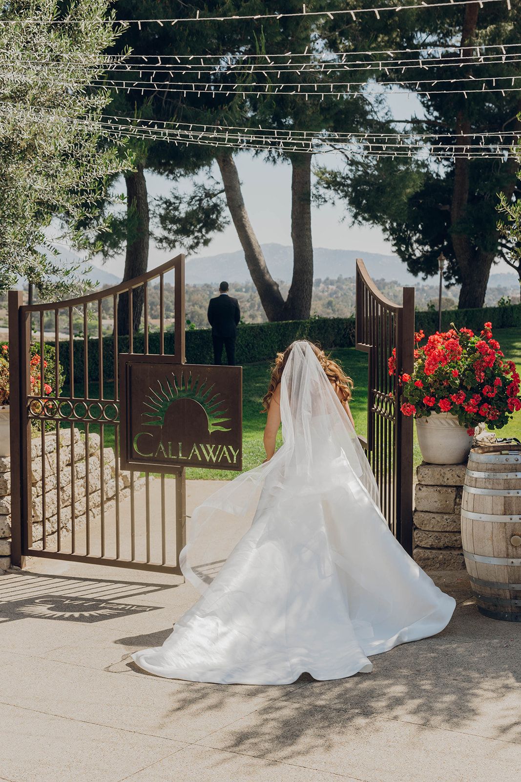 A wedding dress with flowing veil captured at the entrance gate of Callaway Estate with string lights and floral decor.