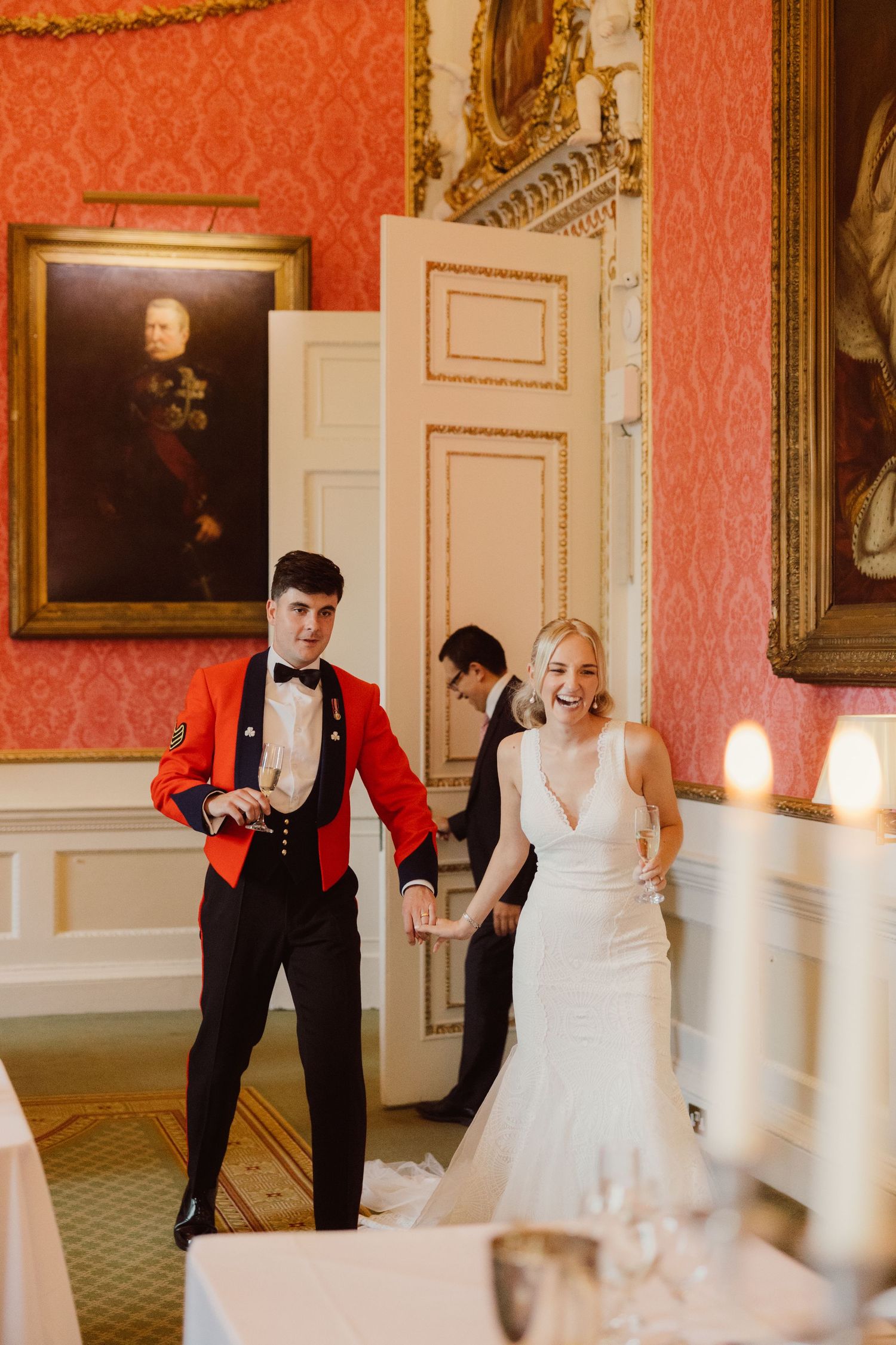Wedding couple shares a playful moment in an elegant room with red damask wallpaper and ornate gold frames.