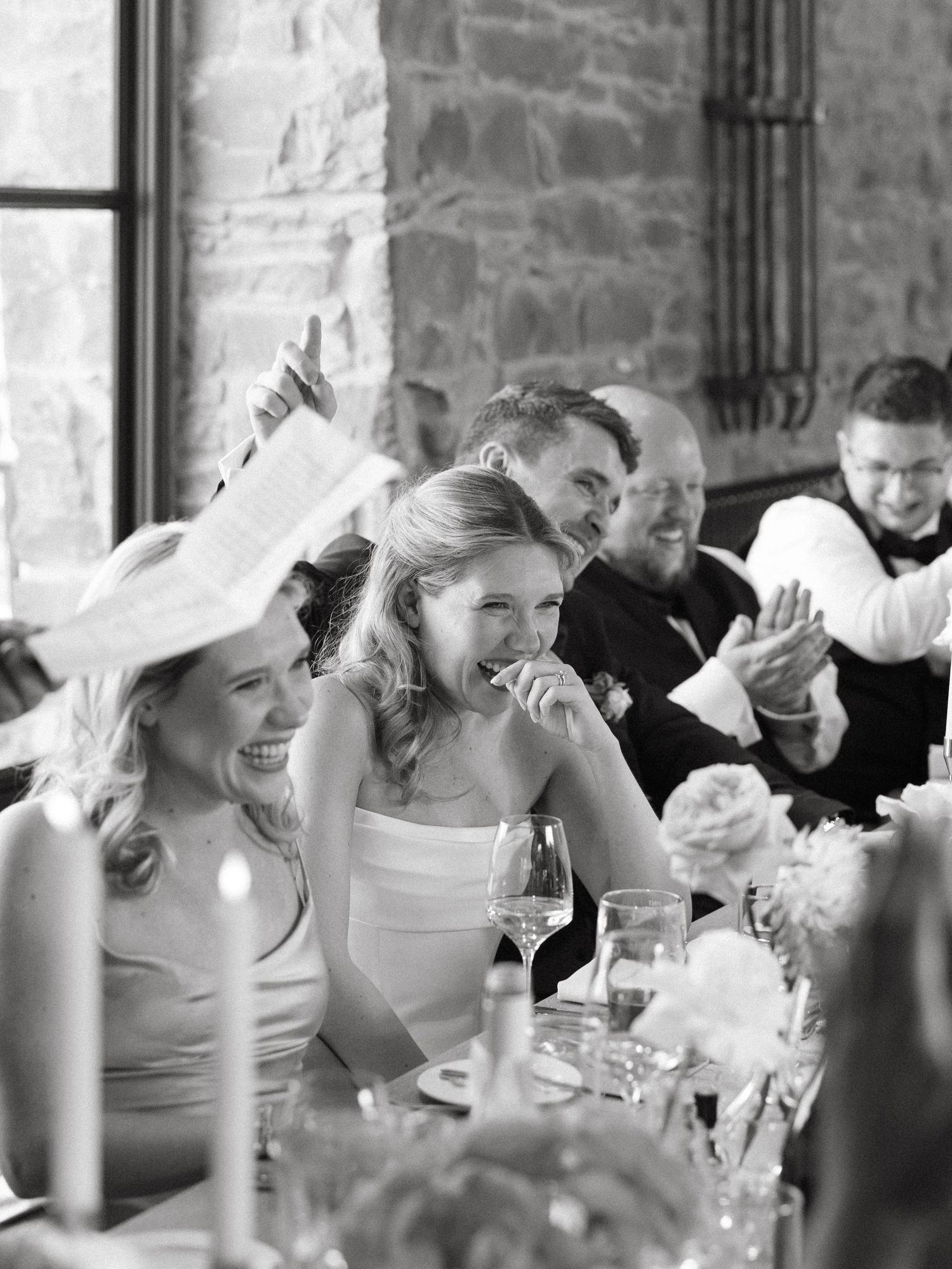 Black and white photo of wedding guests laughing during reception speeches.