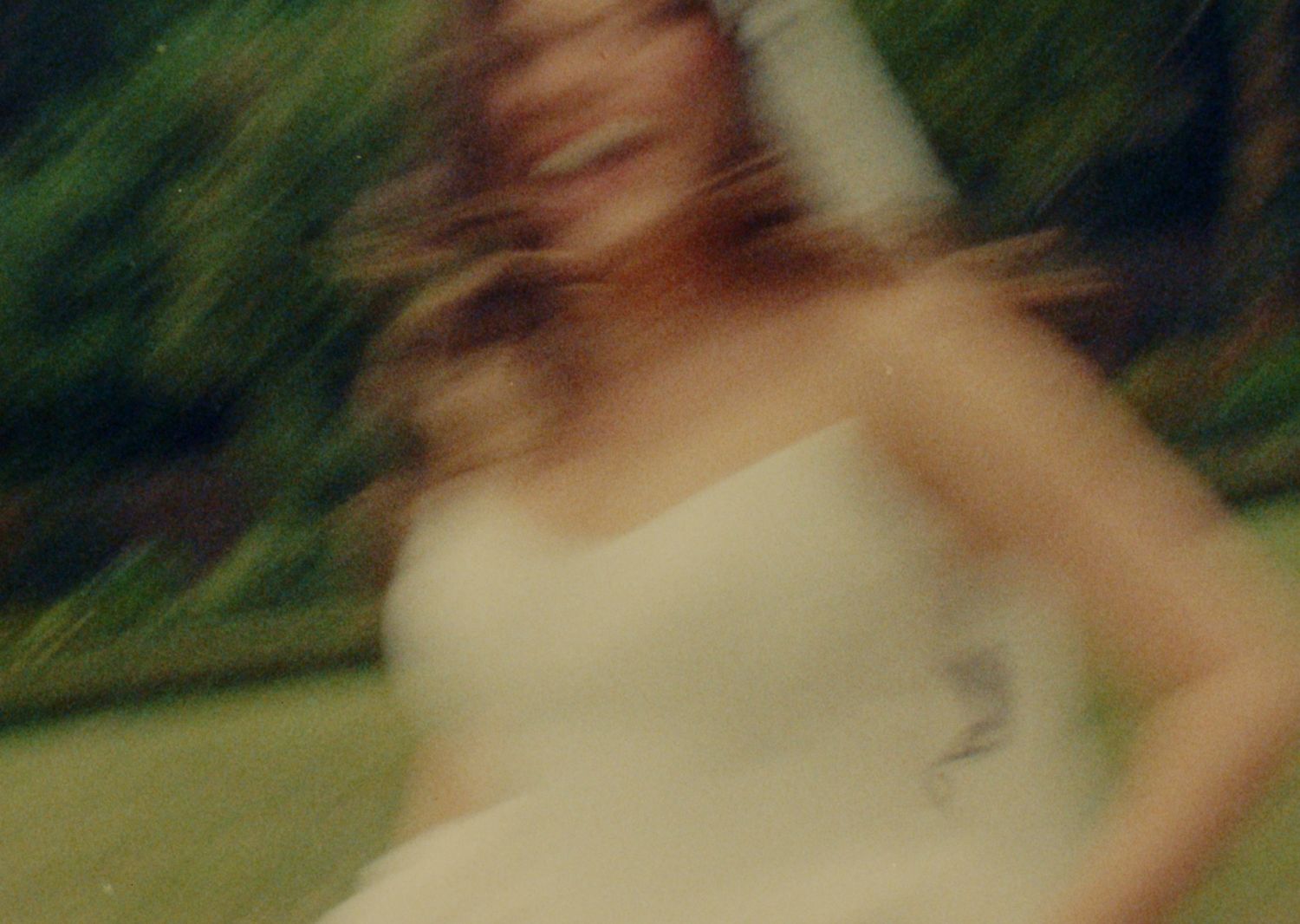 Blurred motion photo of a woman in a white strapless dress spinning outdoors near green trees.