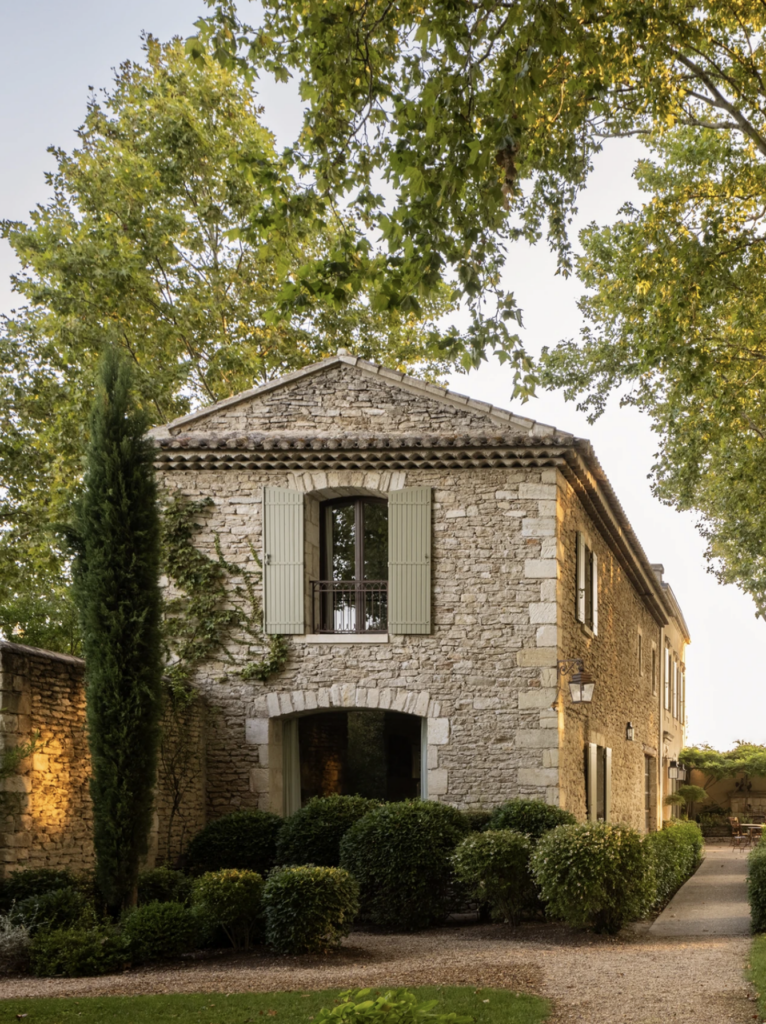 A rustic stone building with shuttered windows and cypress trees set against a golden evening light in Provence.