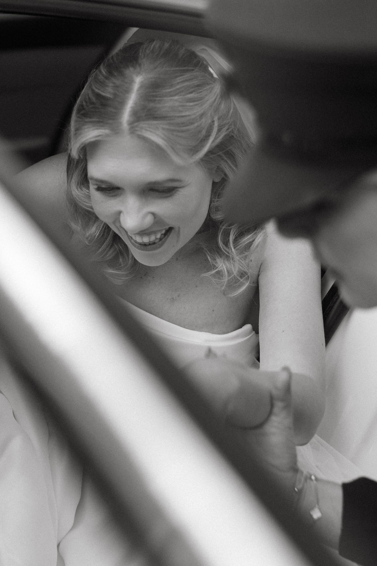 Artistic black and white portrait through window blinds showing joyful expression.