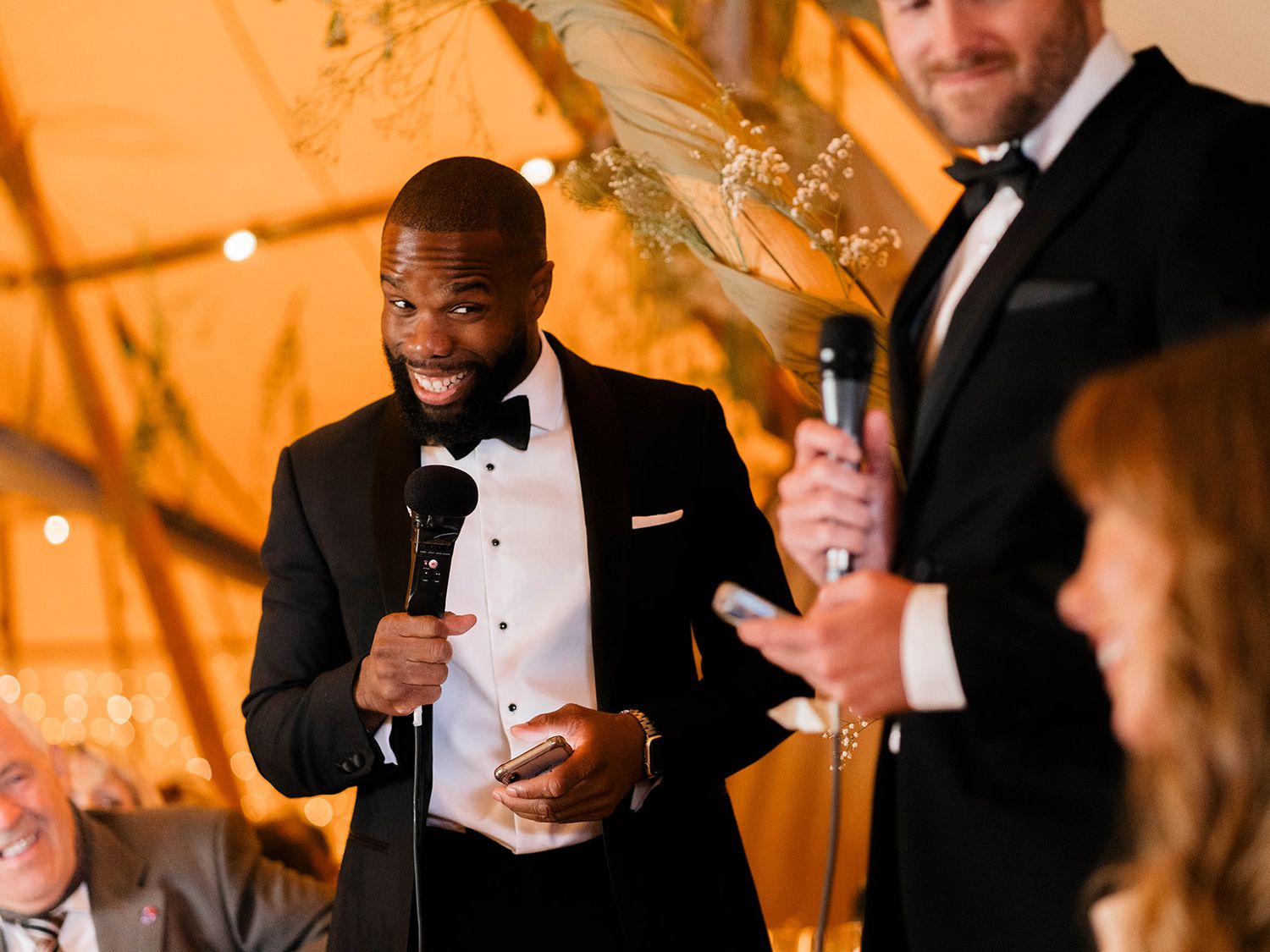 Wedding guests deliver toasts and speeches under warm lighting in an elegant tent reception.