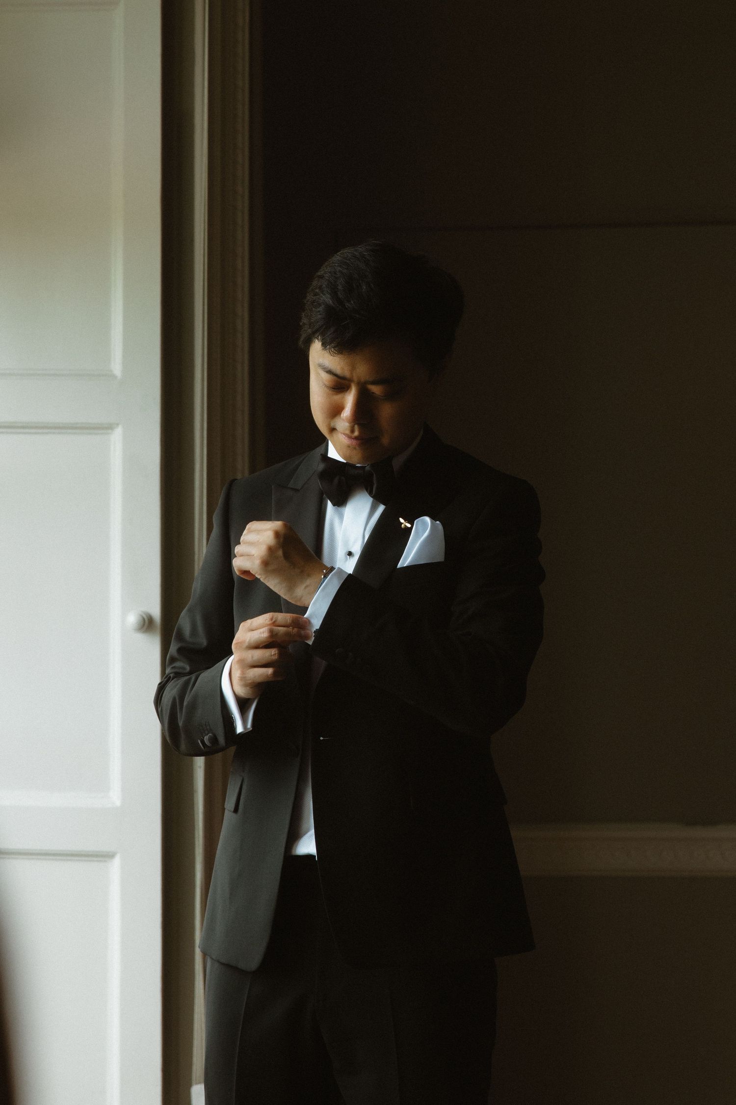 Someone adjusting their cufflinks while wearing a classic black tuxedo.