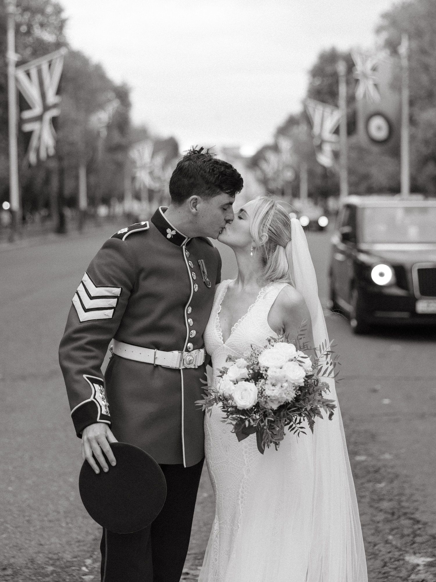 A couple in wedding attire share a romantic kiss outdoors on a cobblestone street.
