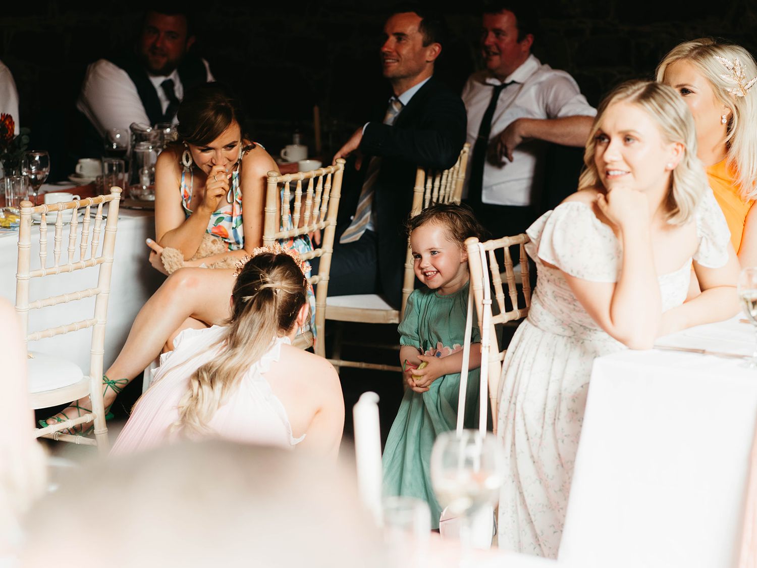 People enjoying a wedding reception while seated at decorated round tables with white chairs.