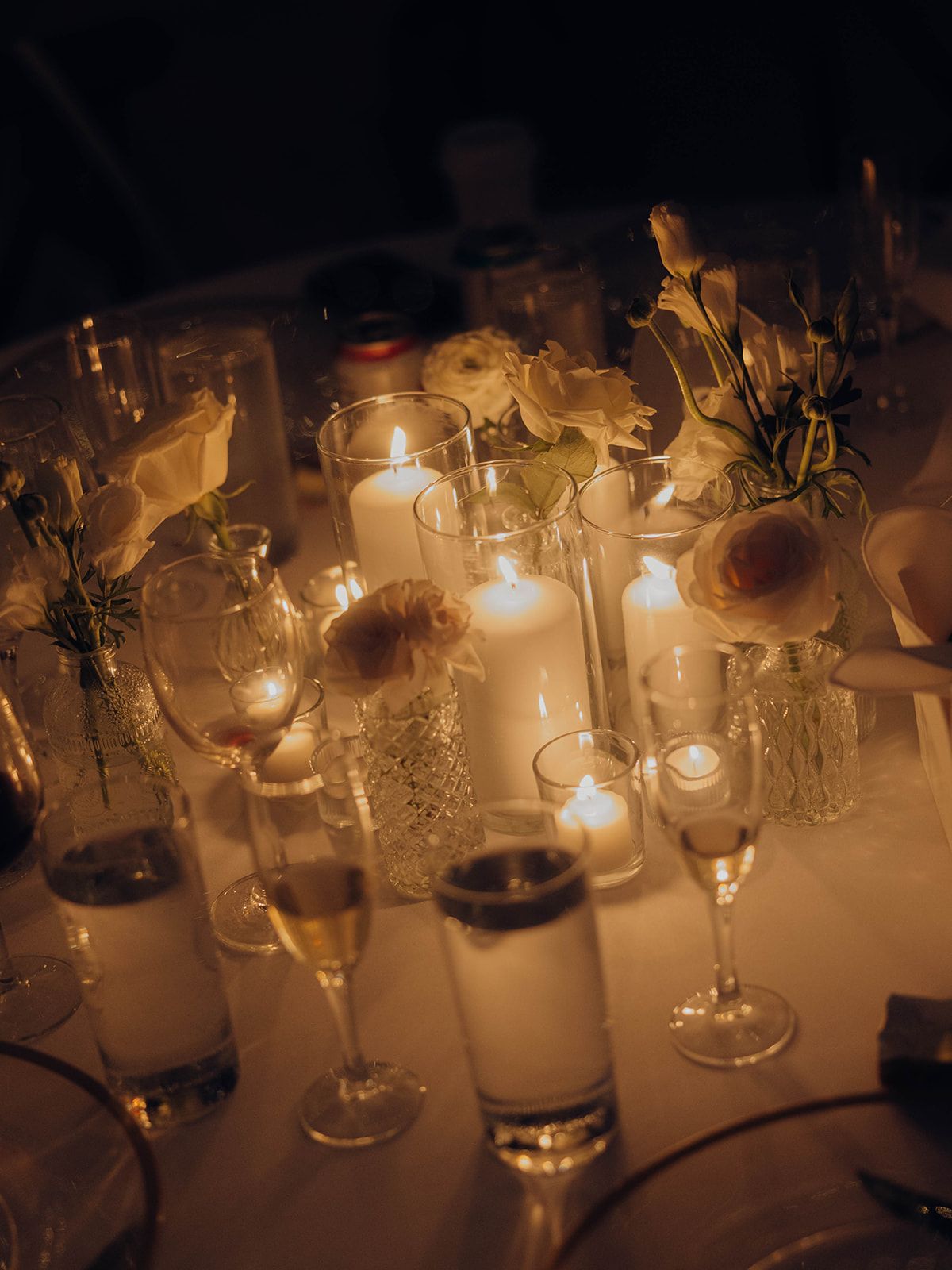 Romantic candlelit table setting with champagne glasses and delicate floral arrangements glowing in warm light.