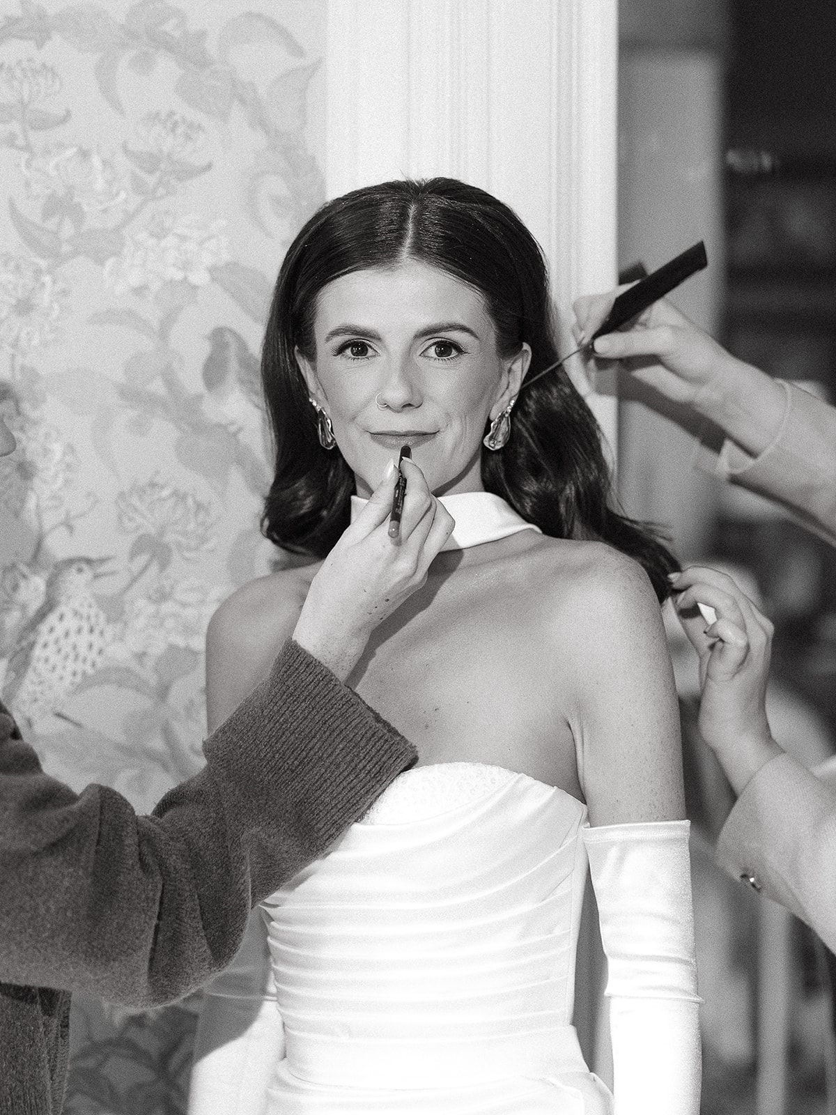 Wedding preparation scene showing makeup application in black and white photography.