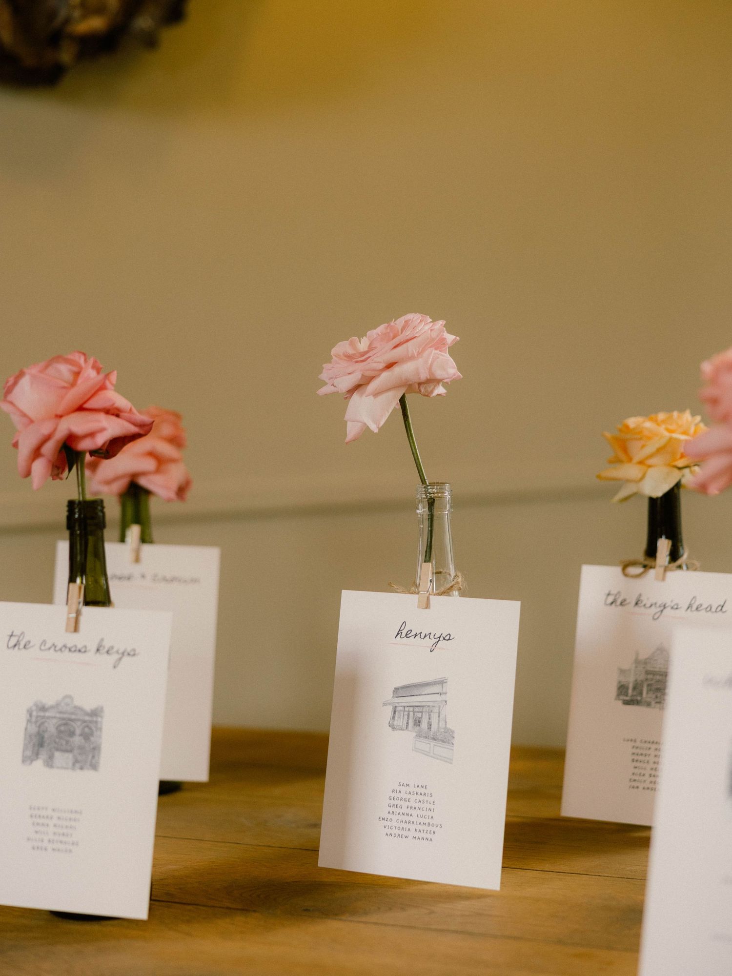 Wedding reception table cards with delicate pink and peach roses in small glass vases display venue illustrations.