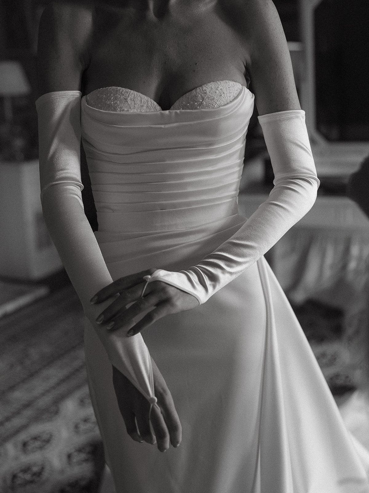 A close-up view of a white wedding dress with elegant long gloves, showing the detailed bodice and waistline.