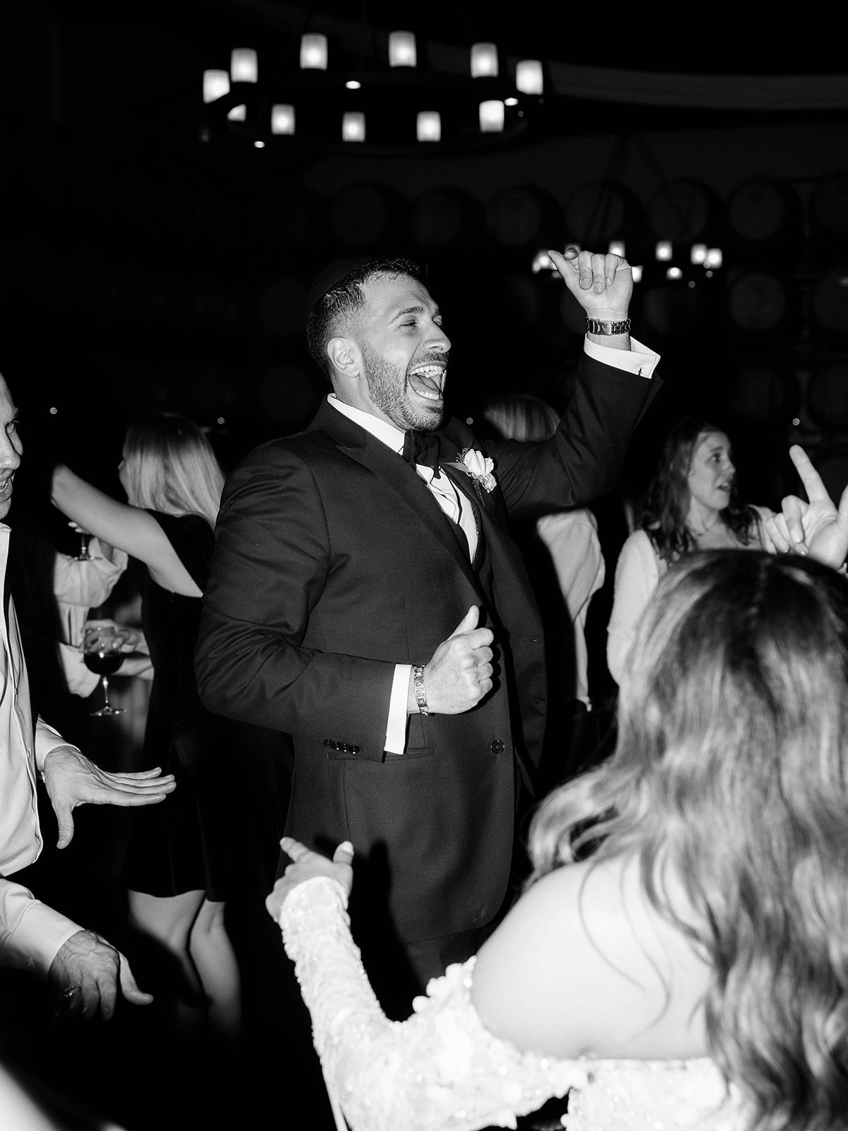 Wedding guests dance and celebrate with joyful energy on a dimly lit dance floor at a reception party.