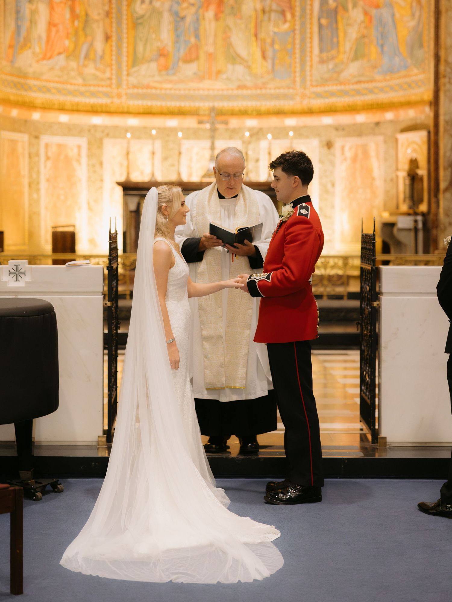 A wedding ceremony takes place in an ornate church with golden curved walls and intricate religious artwork.