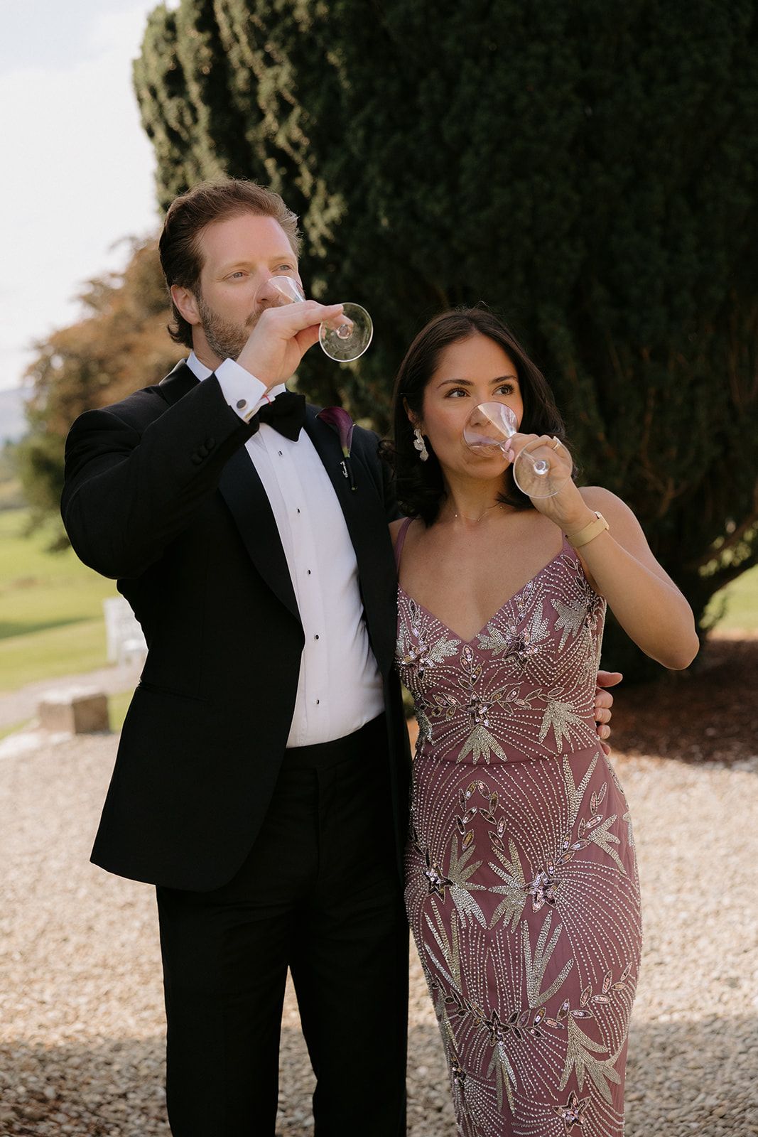 A couple in formal attire shares a drink together during an outdoor photoshoot.