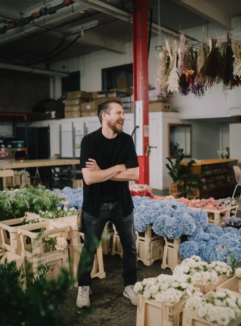 Fresh flowers in brown paper bags being arranged in a warehouse setting with blue hydrangeas and white blooms.