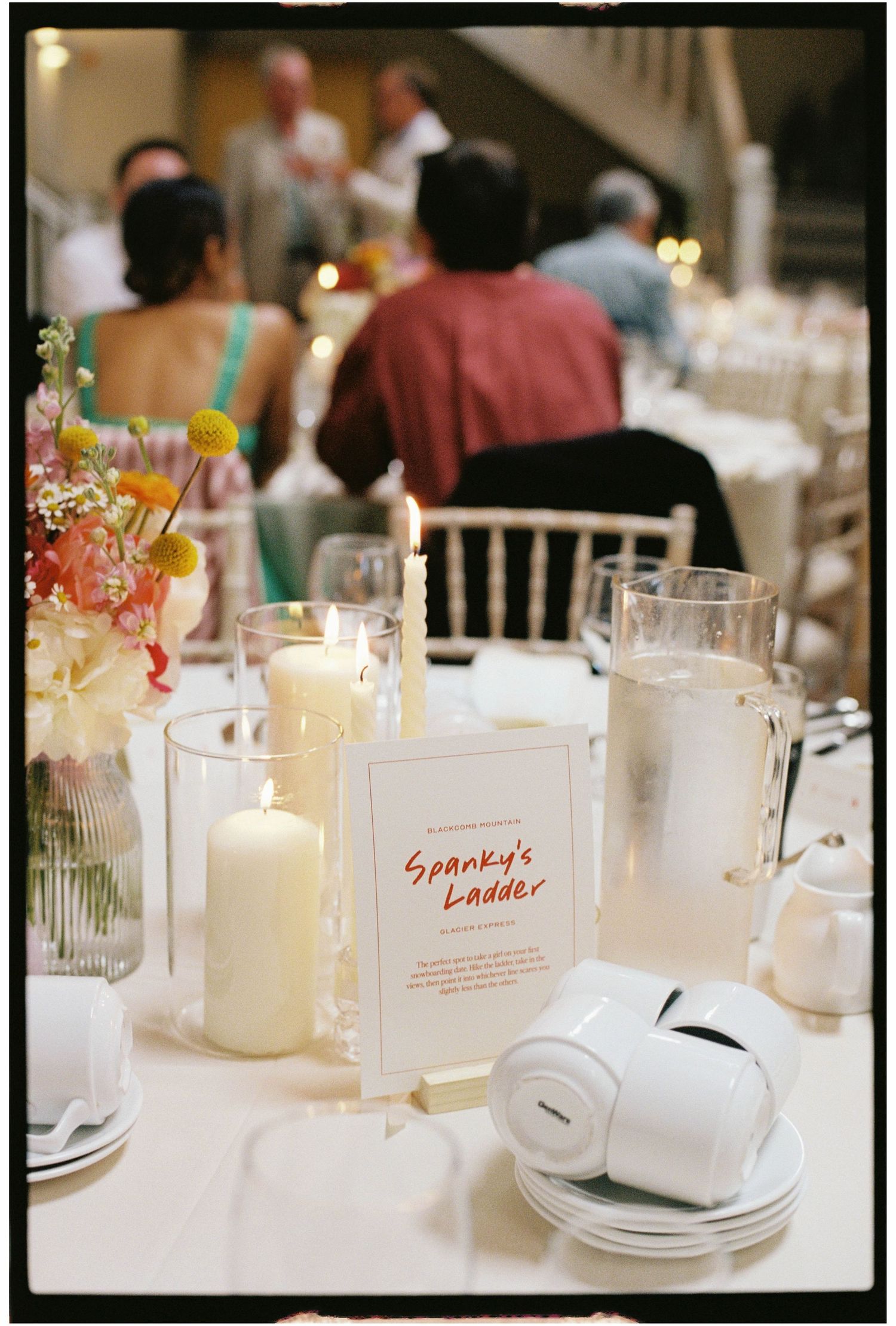 A wedding reception table with white candles, floral centerpiece, and a Spanky's Ladder table name card.