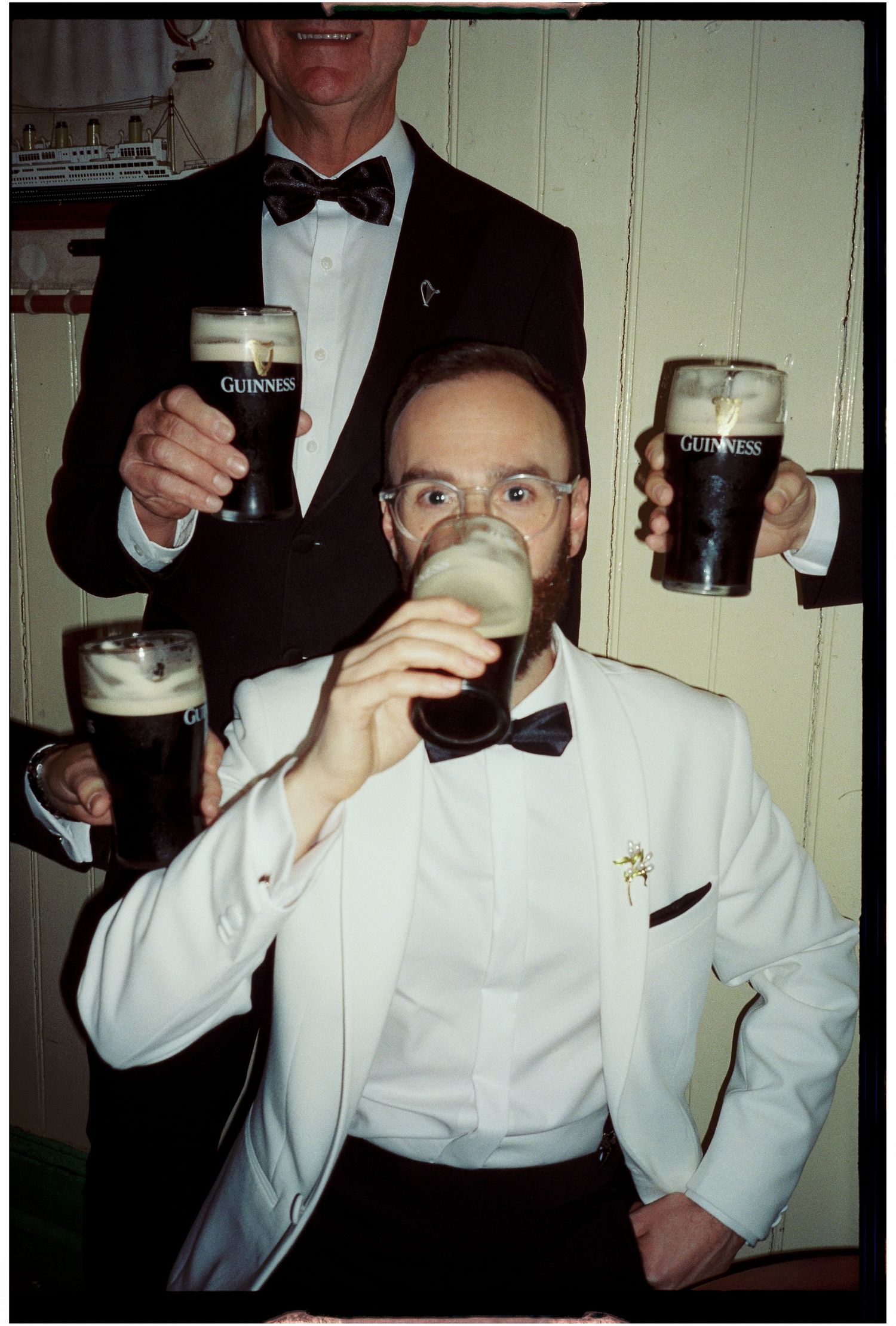 Men in white tuxedo jackets drinking and celebrating at formal event.