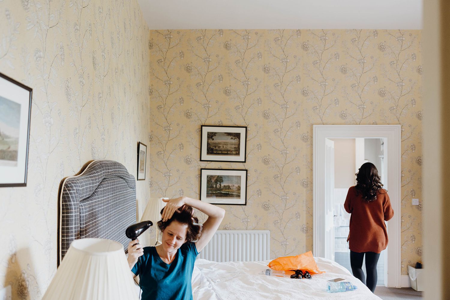 Person stretches against a wall in a bright room with floral wallpaper and framed artwork.