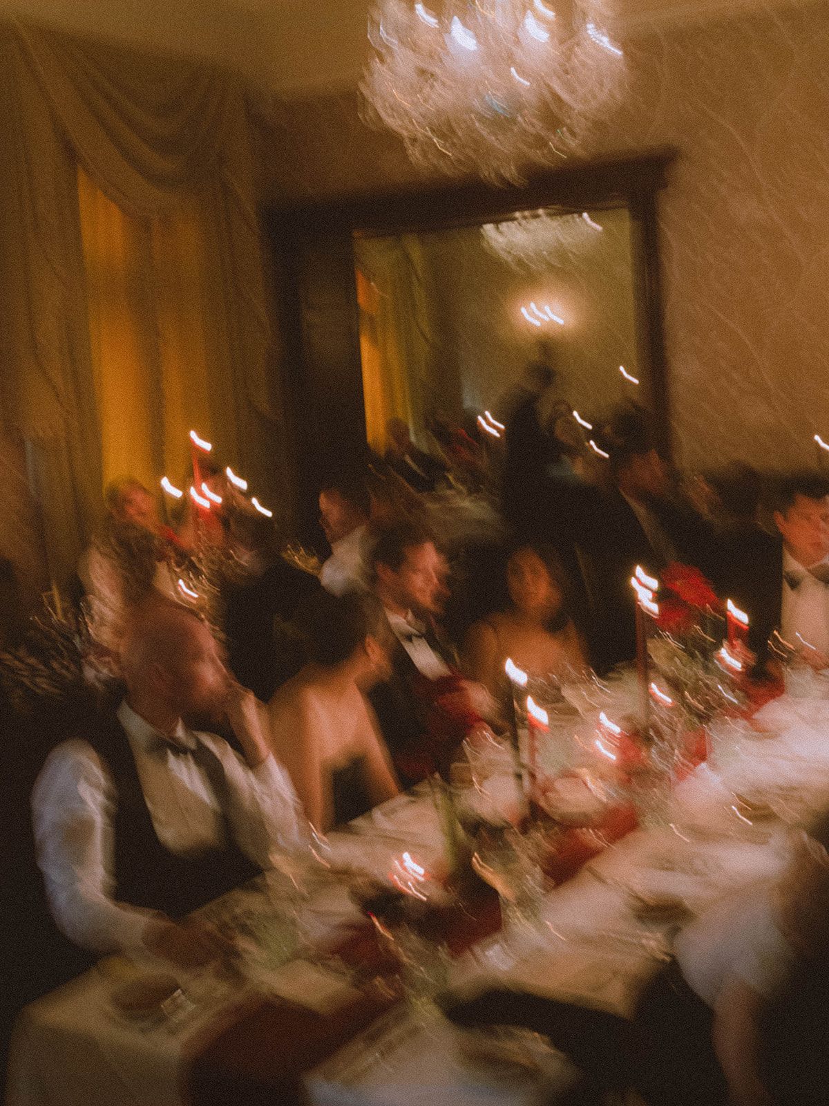 Motion blurred image of people seated in a dimly lit room with warm lighting creating an atmospheric effect.