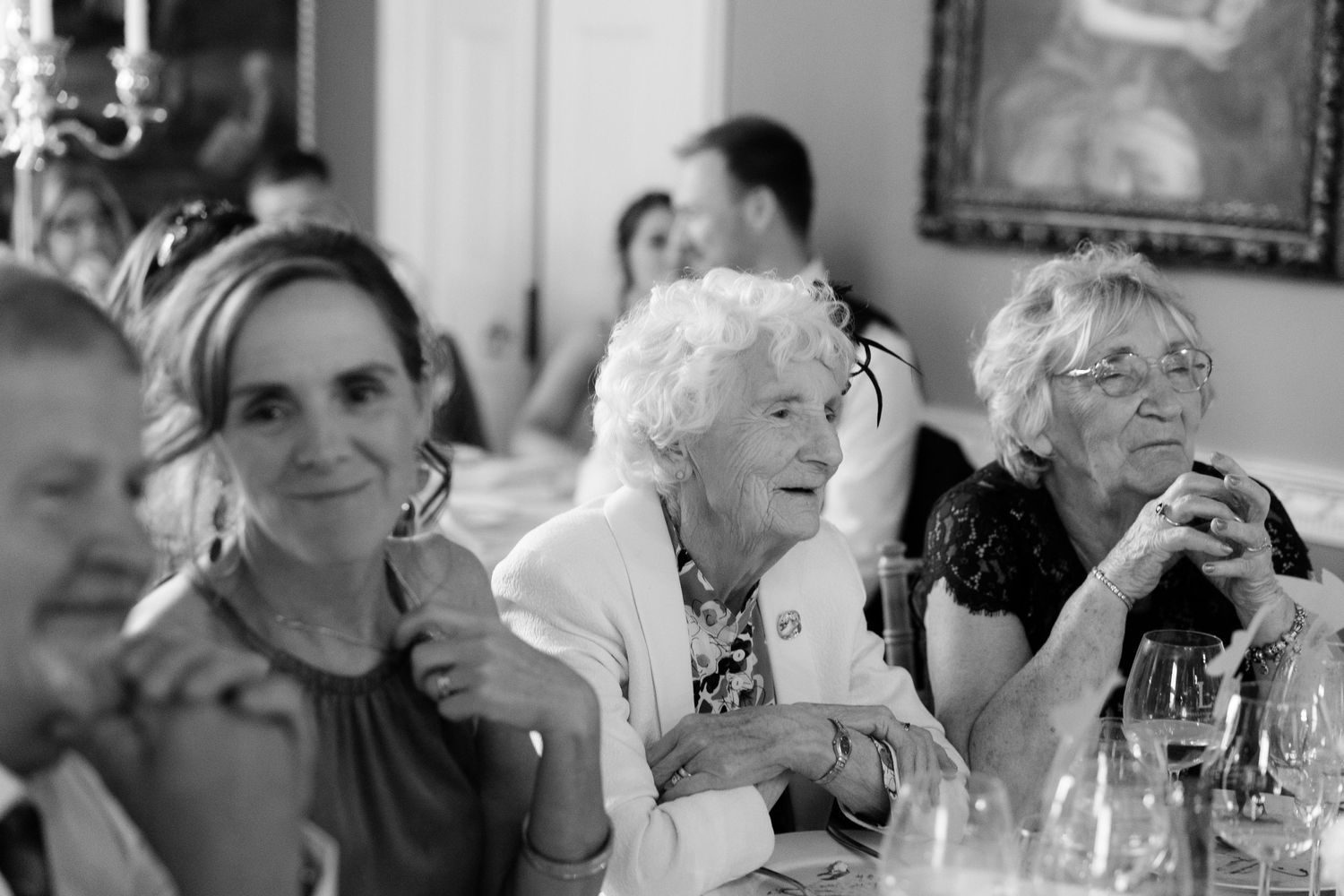 A candid black and white photo of wedding guests laughing and enjoying themselves during a reception dinner.