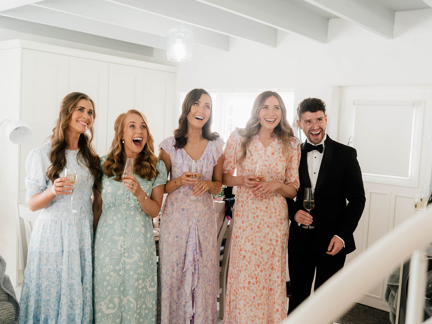Wedding party laughing together in pastel dresses during a candid moment.