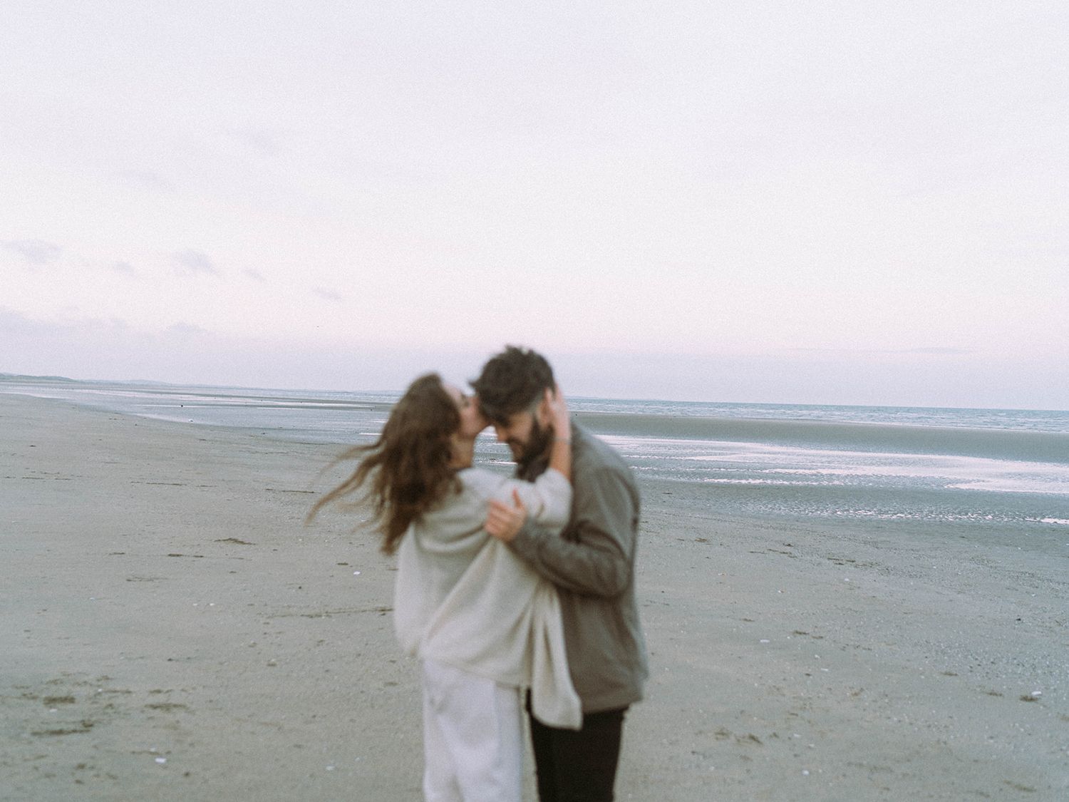 A romantic couple embraces on a misty beach during golden hour.