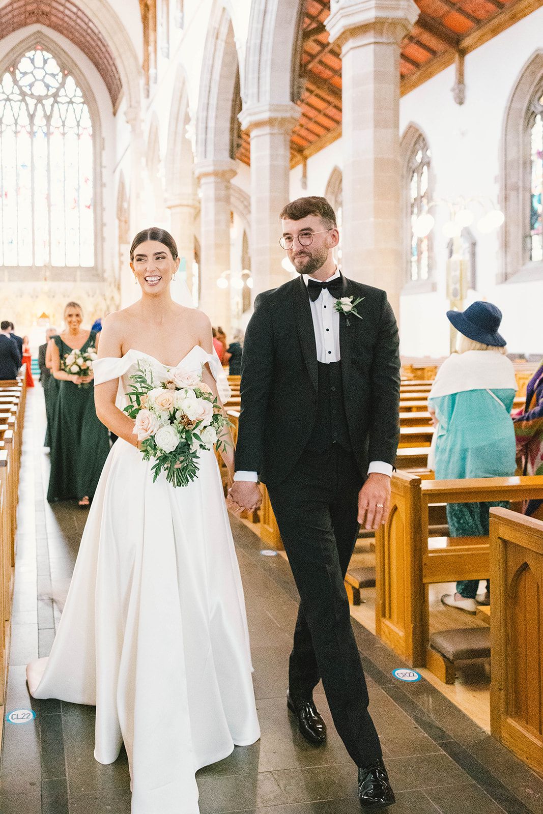 Couple walks down church aisle after wedding ceremony in traditional white dress and black tuxedo.