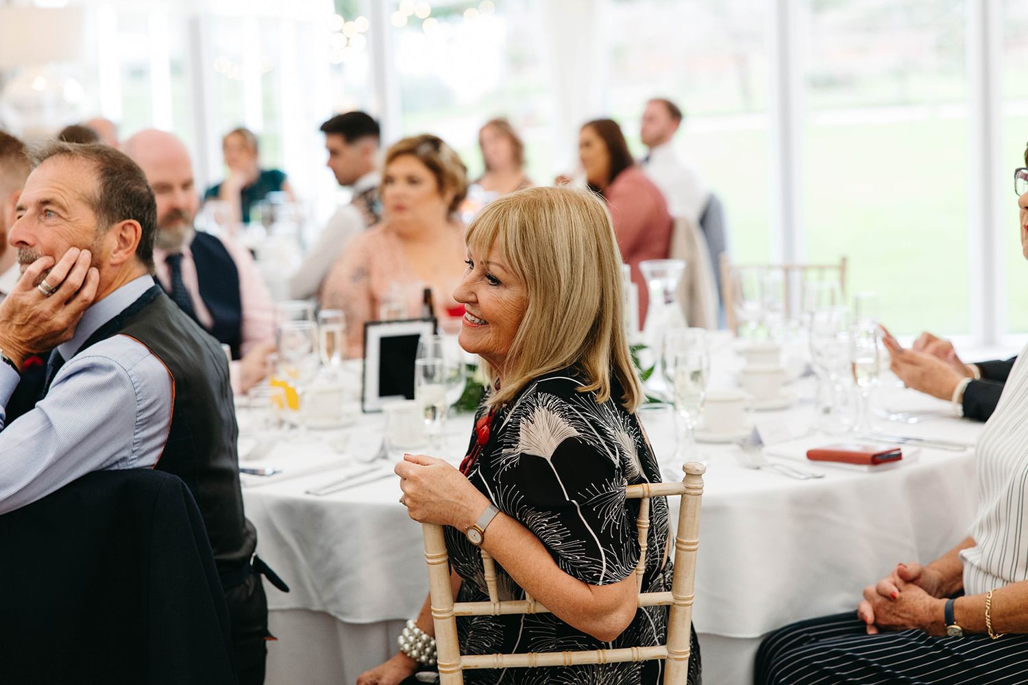 Wedding guests seated at round tables with white tablecloths enjoying drinks during a reception celebration.