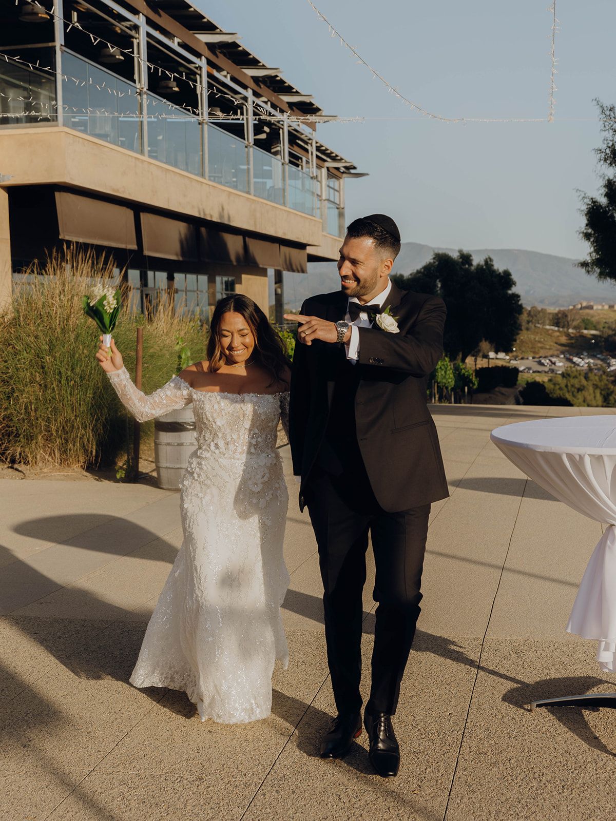 Newlyweds celebrate joyfully on an outdoor terrace in formal attire during their wedding reception.