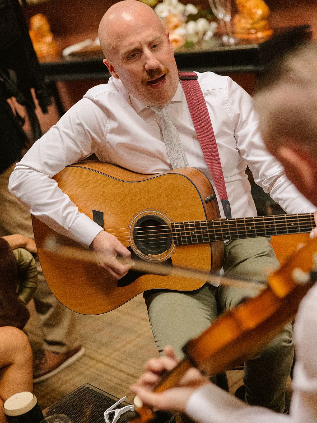 A musician in a white shirt plays acoustic guitar at an intimate venue setting.