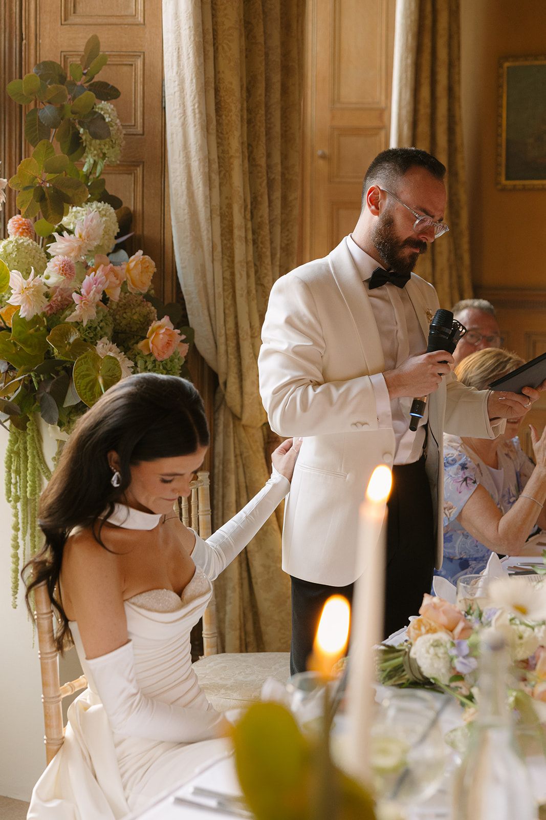 Romantic wedding couple shares tender moments during reception dinner at an elegant venue with floral decorations.