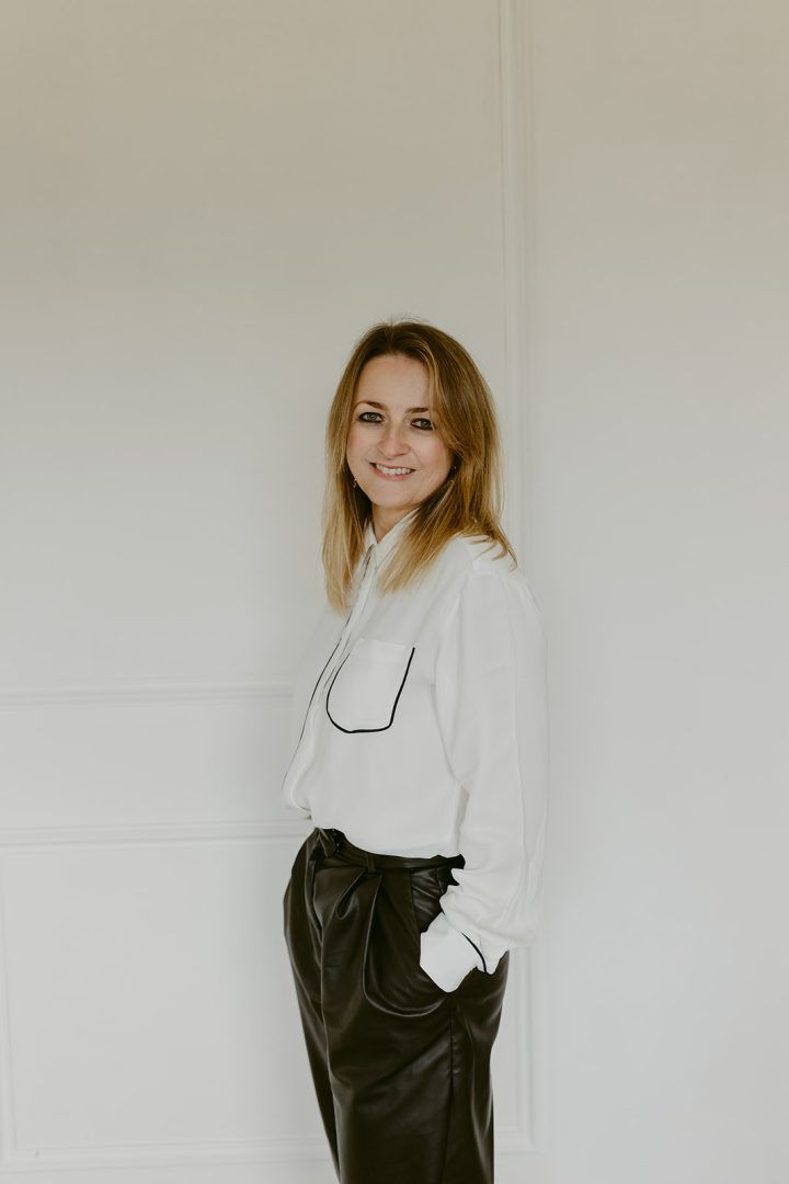 A series of four minimalist portraits against a white wall showing a person wearing a white blouse and black leather dress.