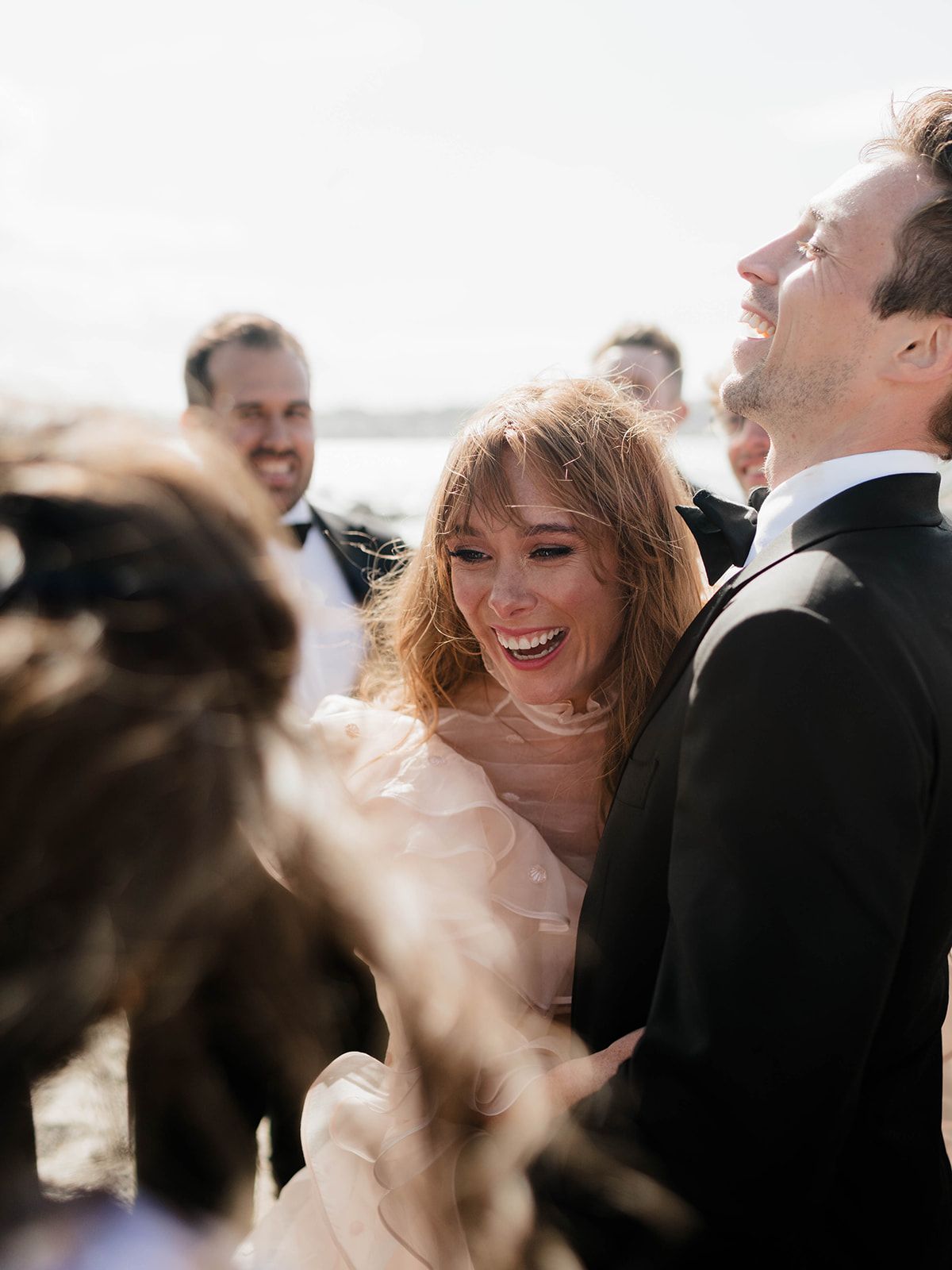 Joyful candid moment between wedding couple and guests during beach celebration.