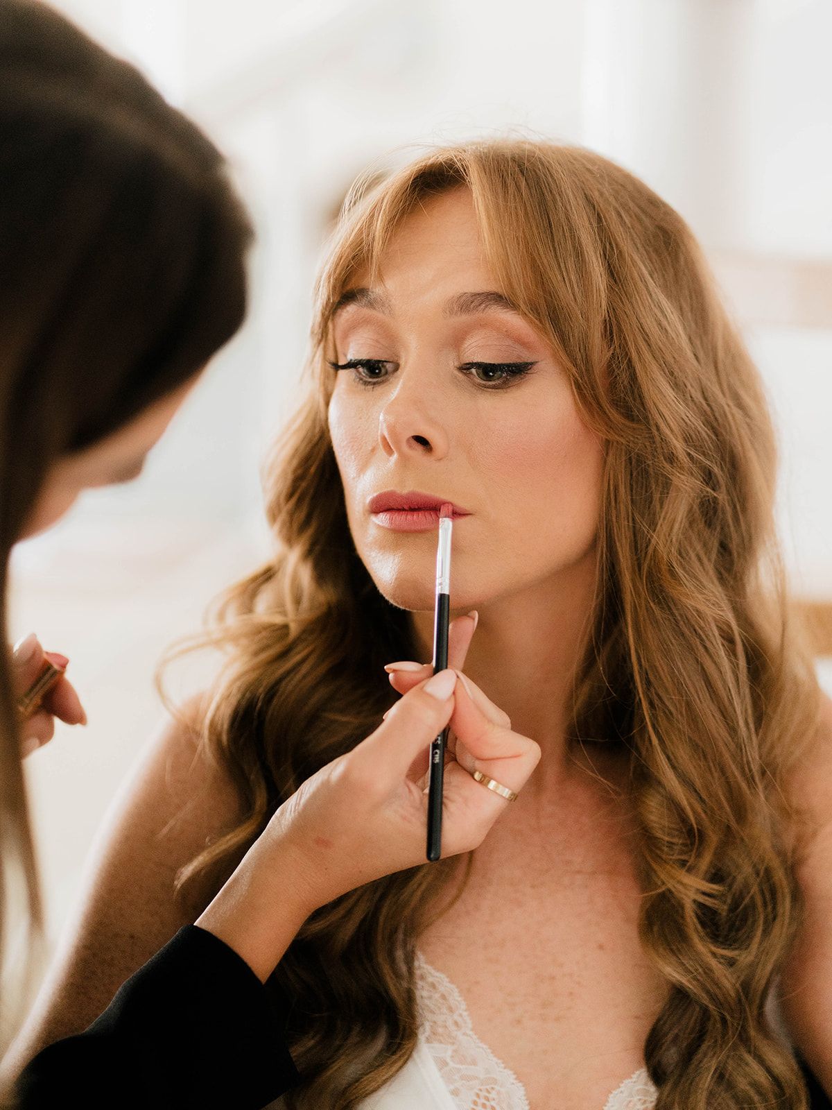 A makeup artist applies lip color during wedding day preparations.
