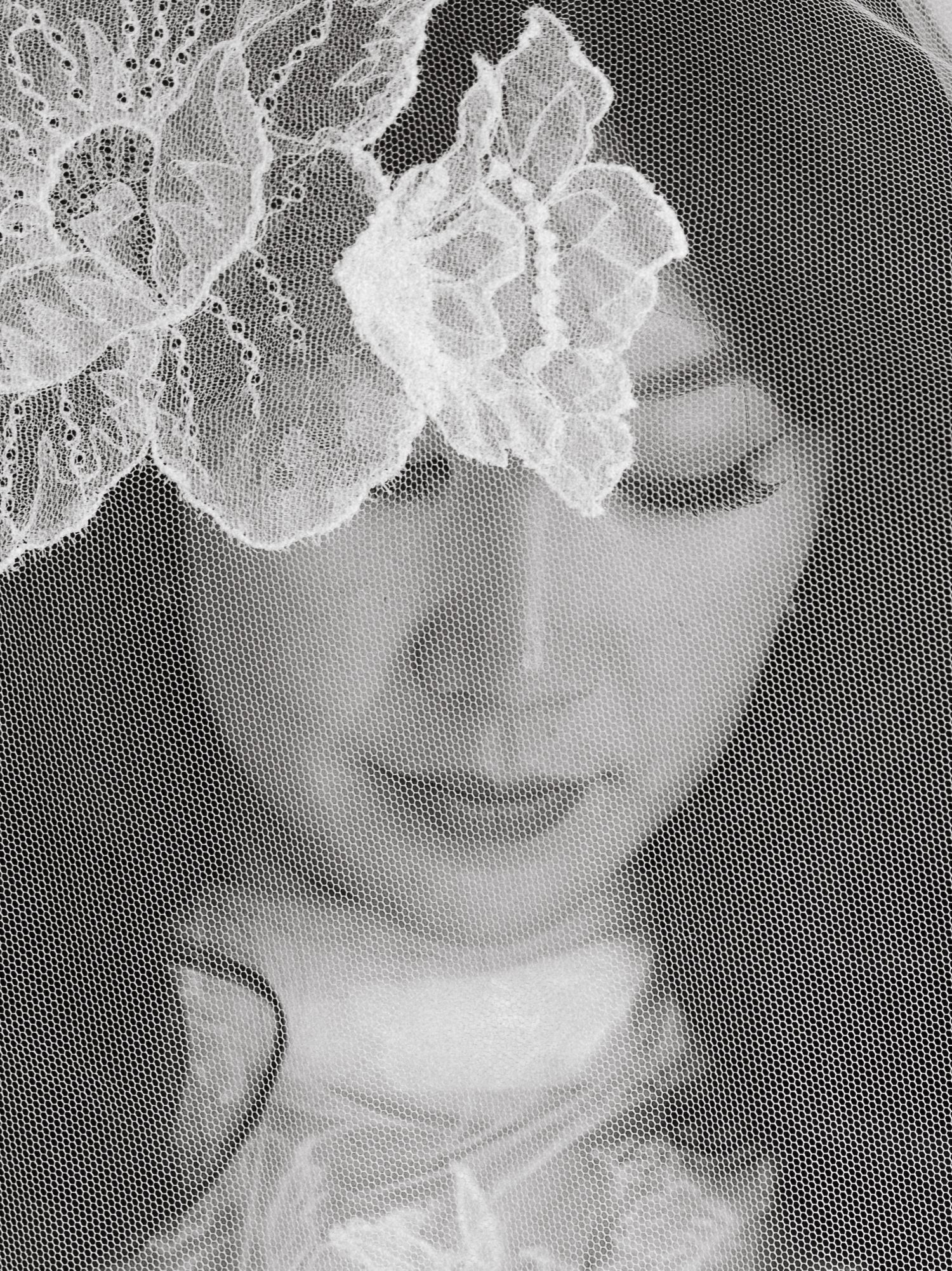 Black and white portrait of a bride wearing an elegant lace veil with floral detail, eyes downcast.